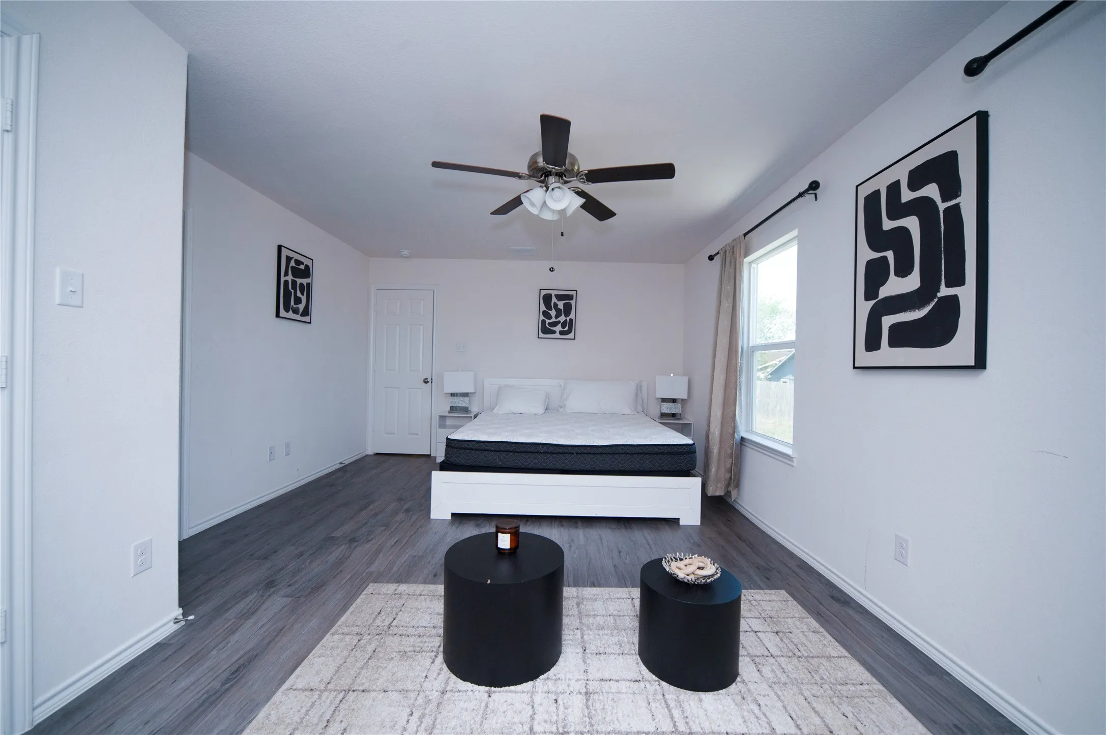 Wood-finish flooring, ceiling fan, white paneled door, and window with curtain rod