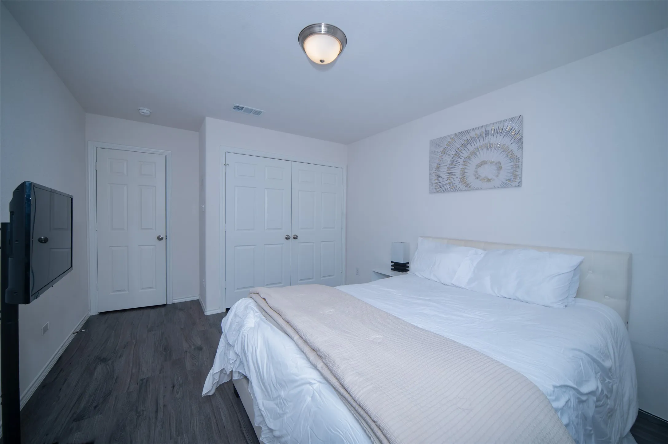 Wood-finish flooring, white paneled doors, ceiling-mounted light fixture, and built-in closet with bi-fold doors