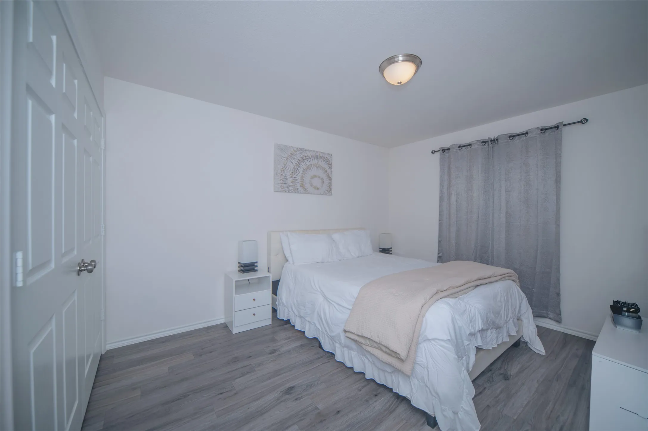 Laminate wood-finish flooring, white paneled door, flush-mount ceiling light, window with curtain rod