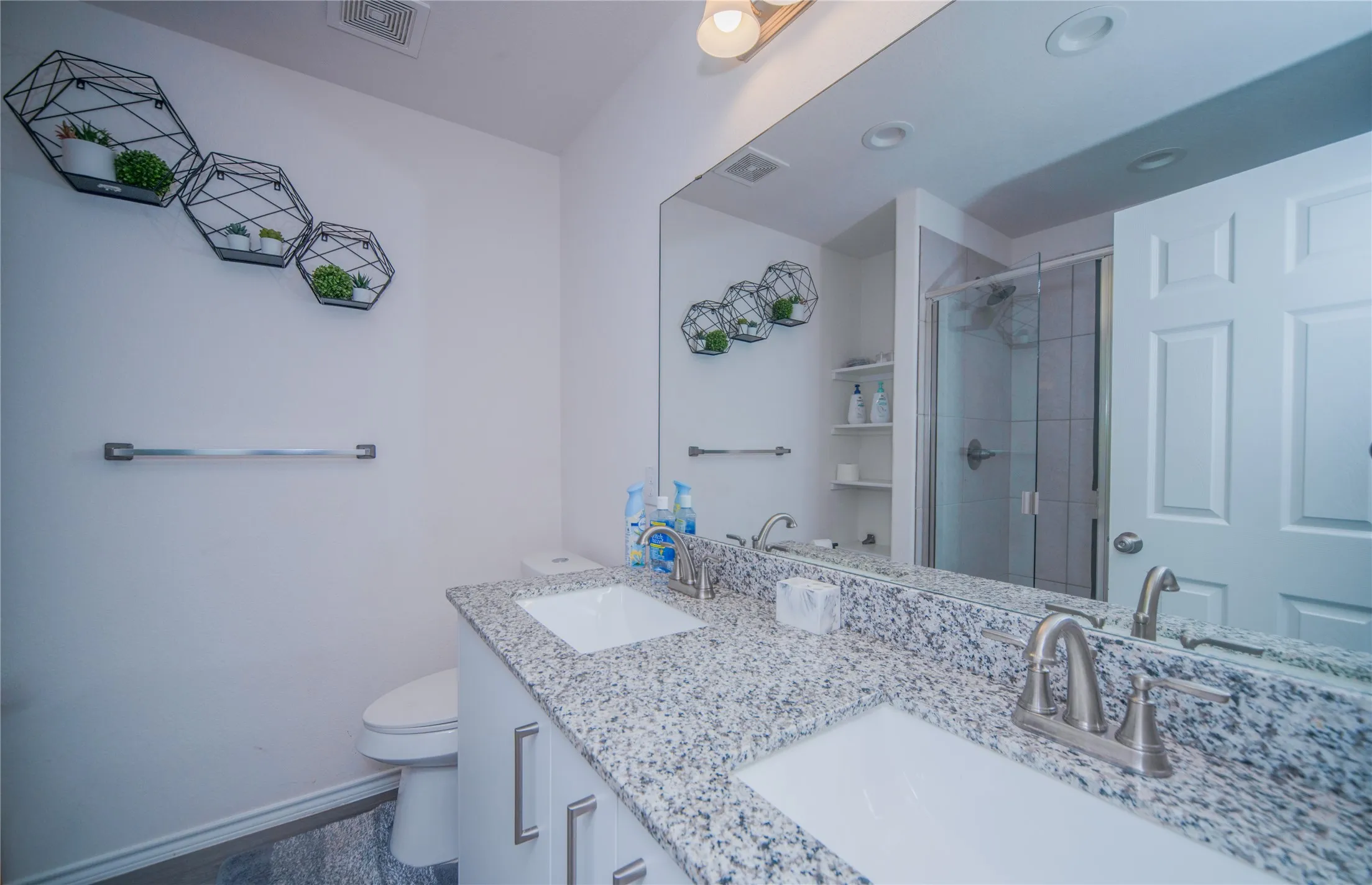 Double vanity with granite countertop and dual undermount sinks, full-width mirror, and a glass-enclosed shower
