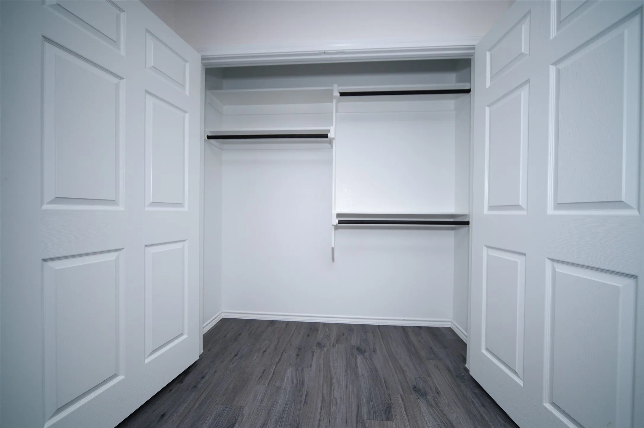 Recessed closet with white shelving, dark wood-finish flooring, and panel doors