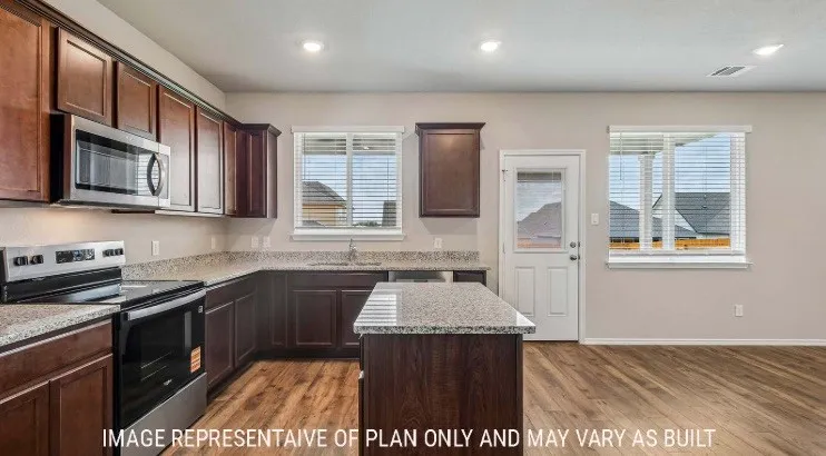 Kitchen featuring wood-finish flooring, dark wood cabinetry, granite-style countertops, stainless steel appliances, and an island