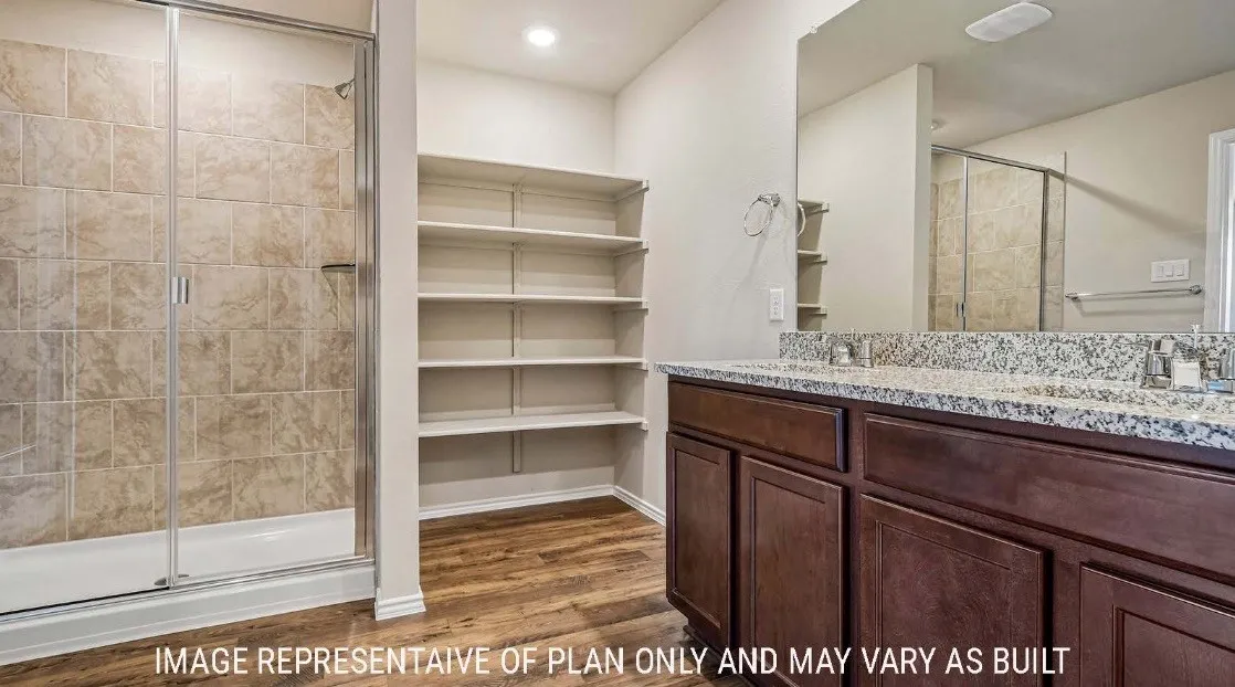 Spa-inspired primary bathroom featuring a dual vanity with granite countertop, rich wood cabinetry, and chrome fixtures