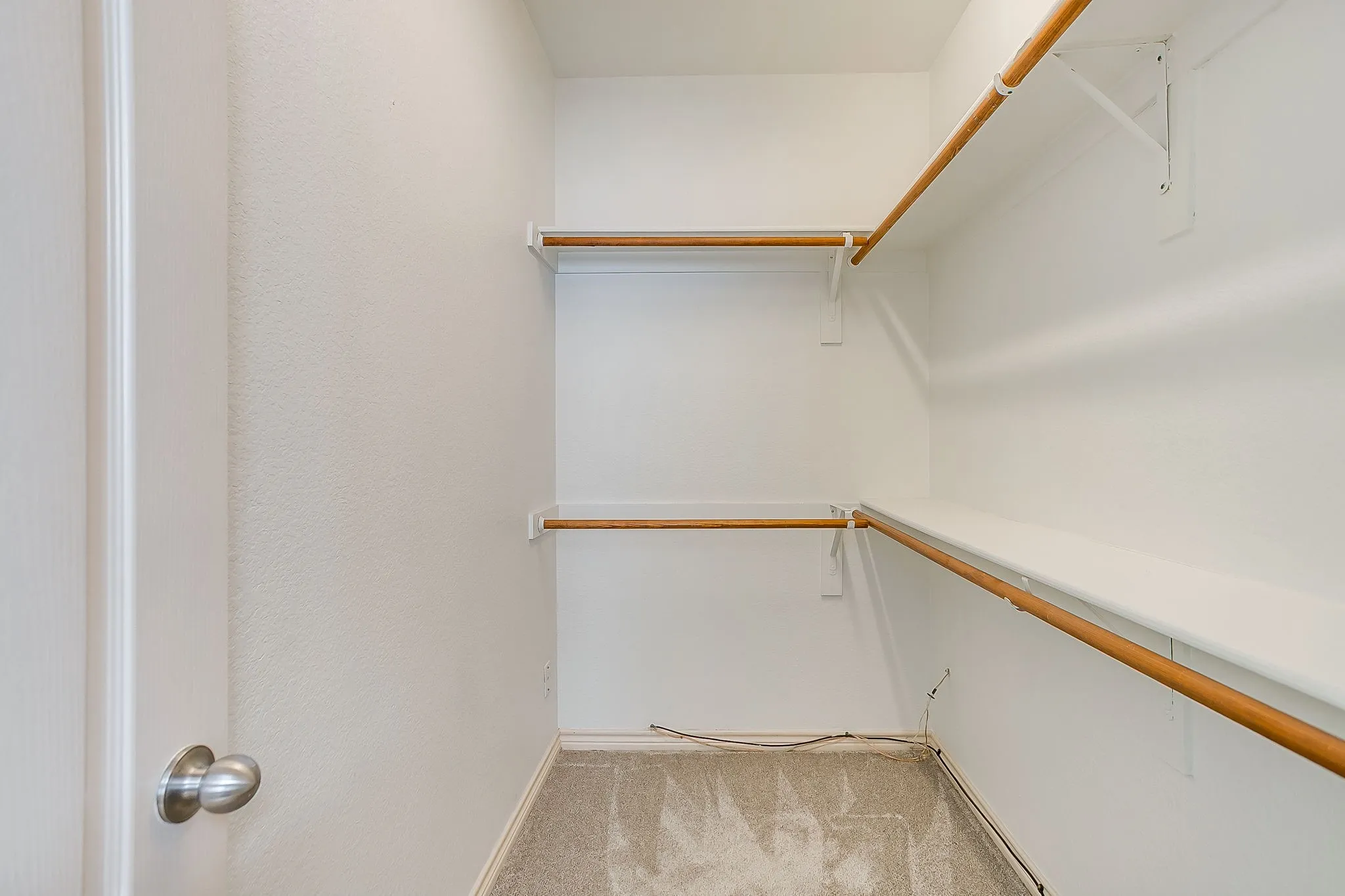 Walk-in closet with carpet flooring, multiple wooden hanging rods, and white shelving