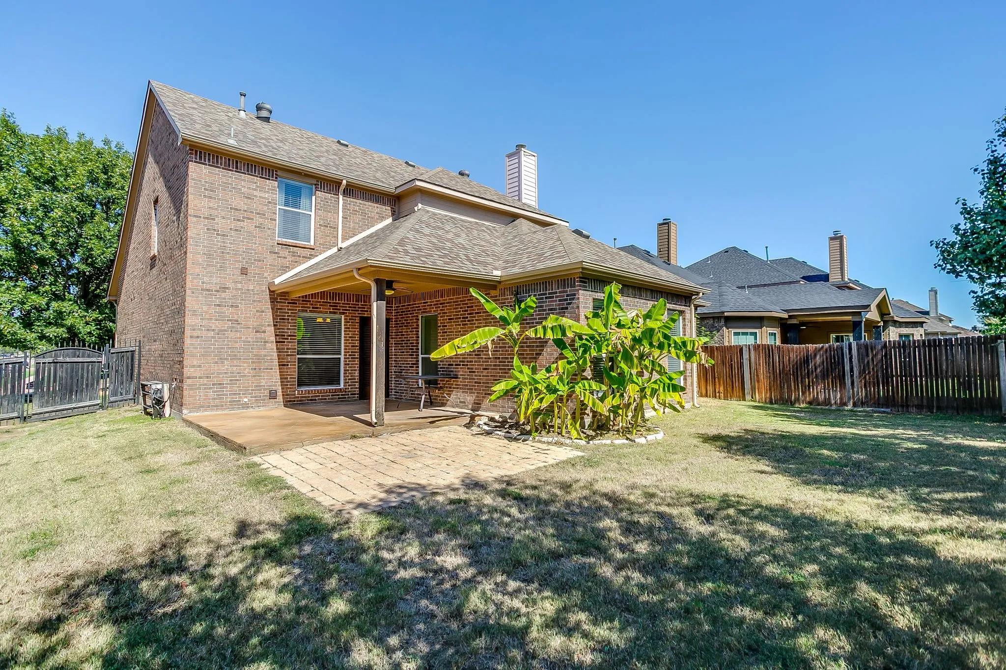 Brick exterior featuring a covered patio, additional paved patio area, and a fenced yard