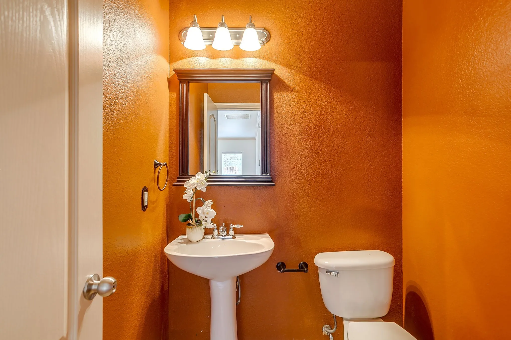 Pedestal sink with chrome faucet, framed mirror, and three-bulb vanity light fixture