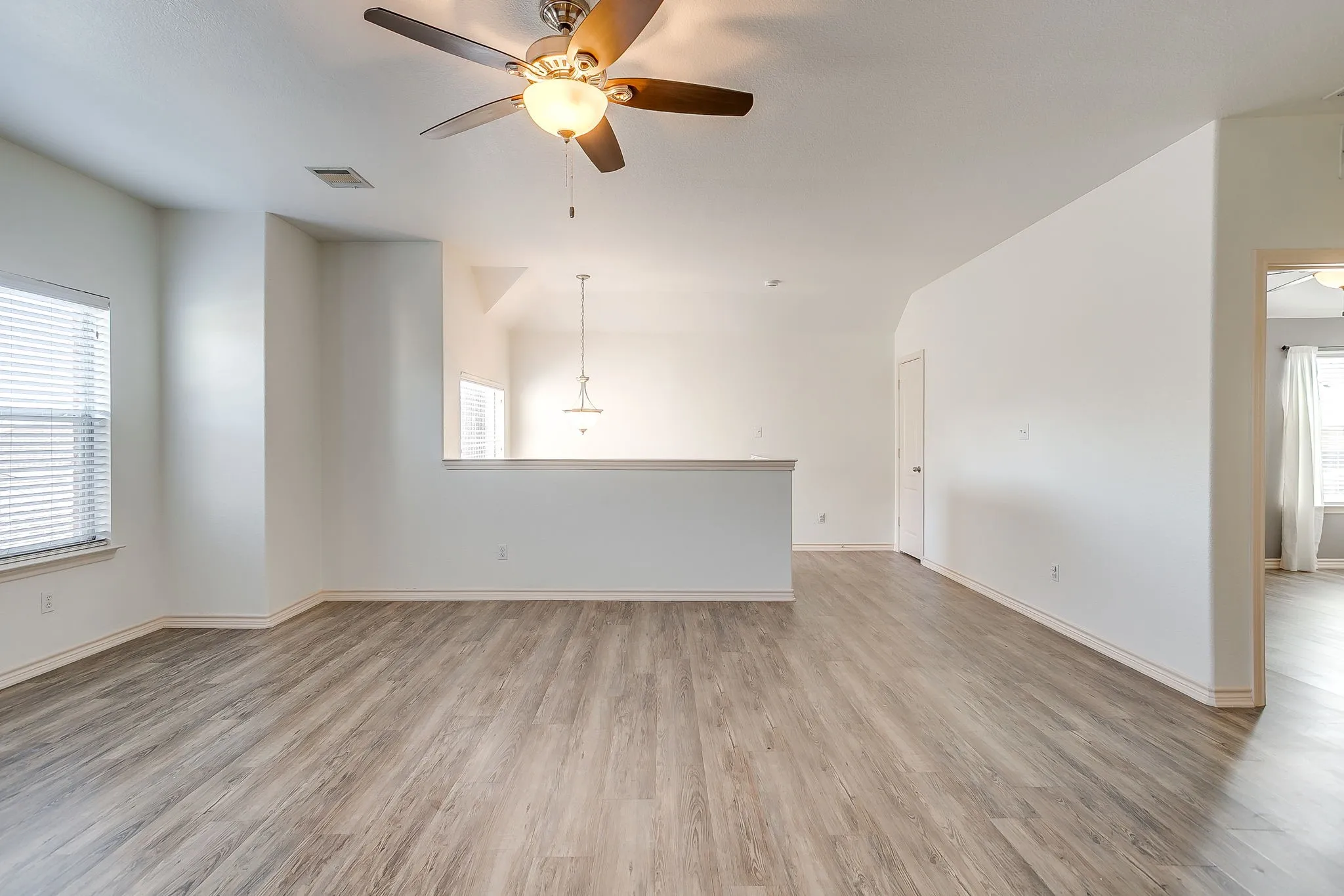 Spacious room featuring wood-finish flooring, white walls, and a ceiling fan with integrated lighting
