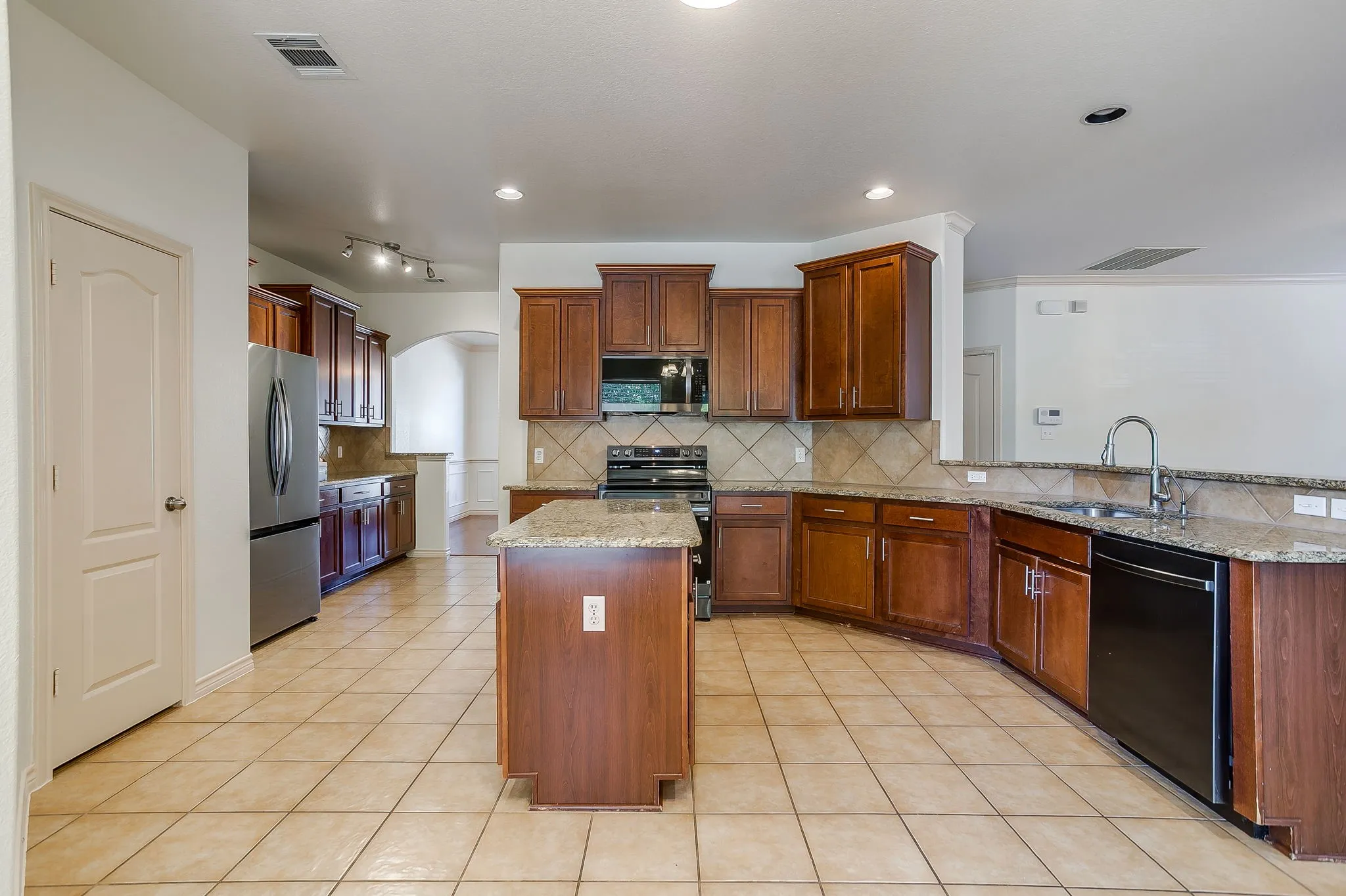 Spacious kitchen featuring an island, tile flooring, wood cabinetry, stone countertops, and stainless steel appliances