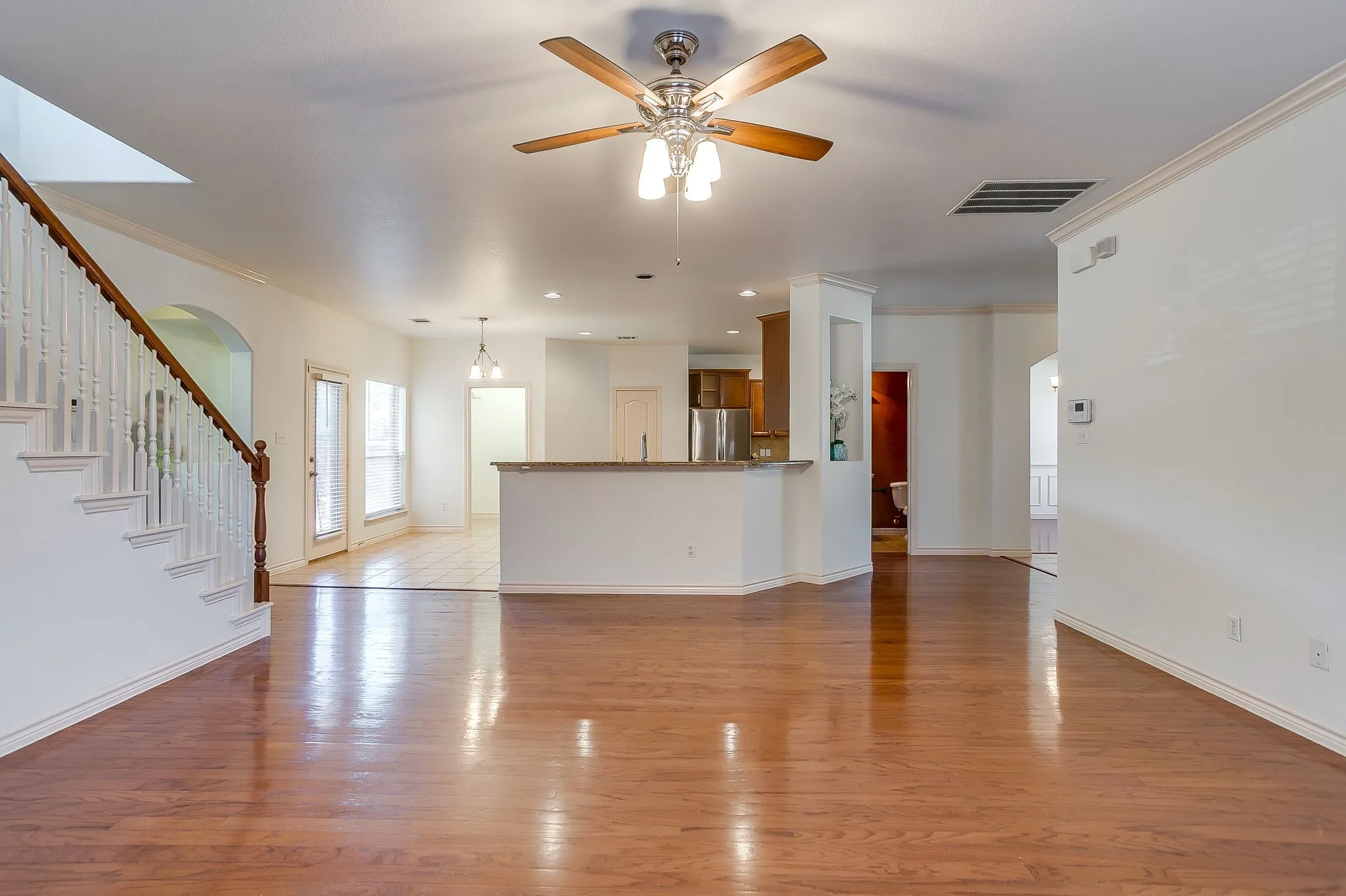Wood-finish flooring, staircase with wood handrail, ceiling fan with integrated lighting, recessed lighting, and crown molding
