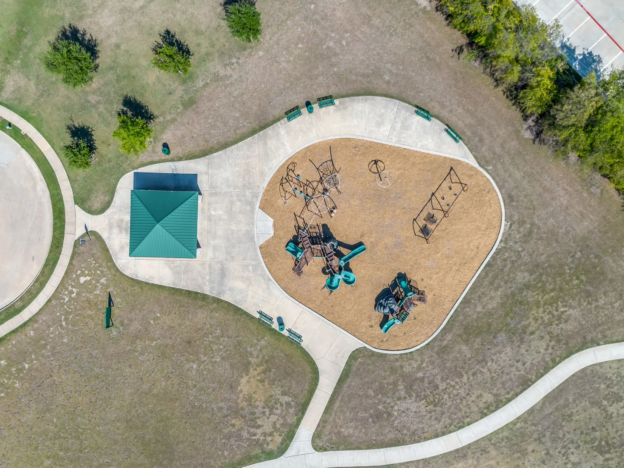 Community park featuring a green-roofed pavilion, playground with multiple structures, and paved walking paths