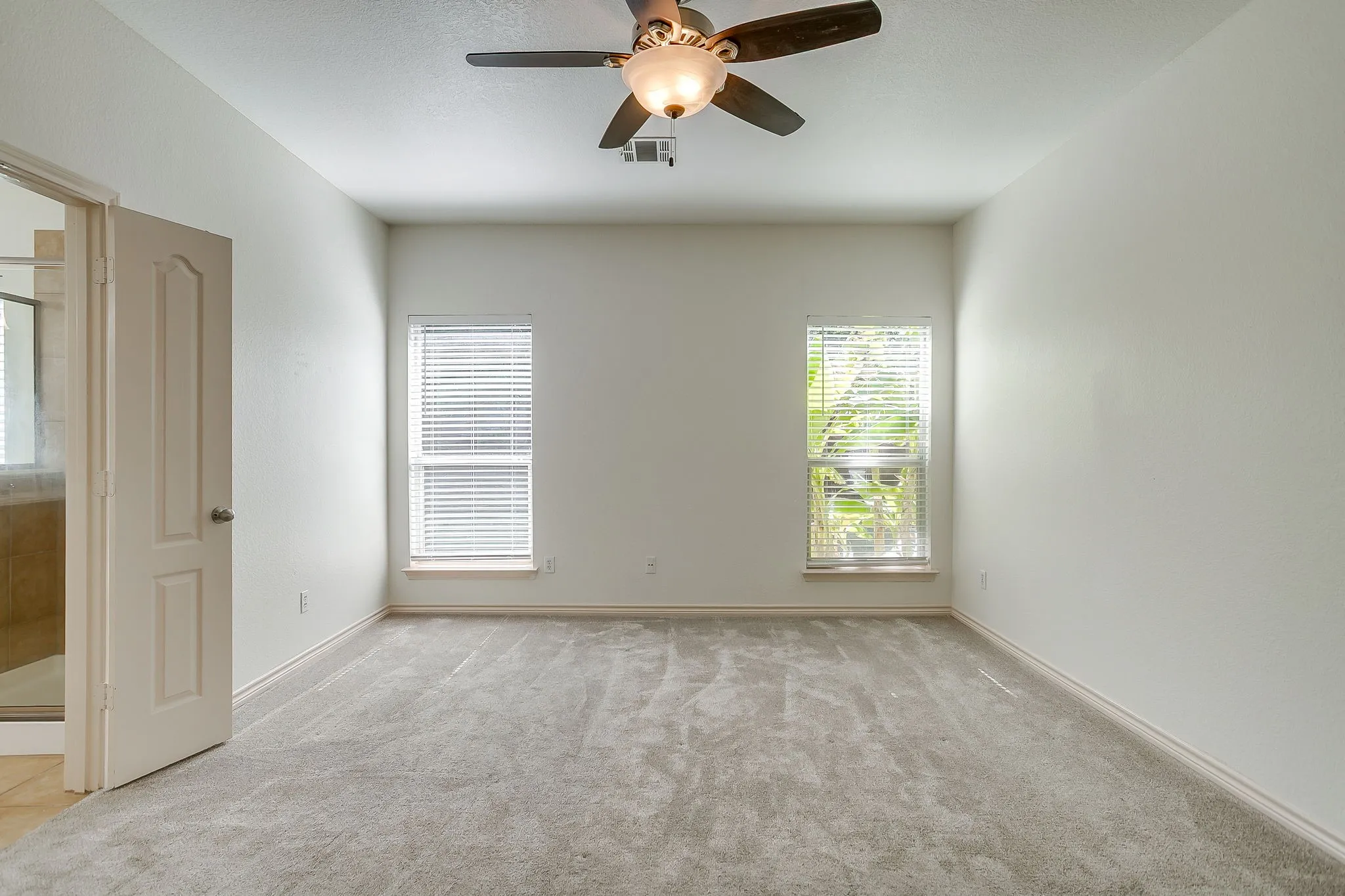 Spacious room featuring neutral carpeting, two windows with blinds, a ceiling fan with integrated lighting, and a neutral wall color