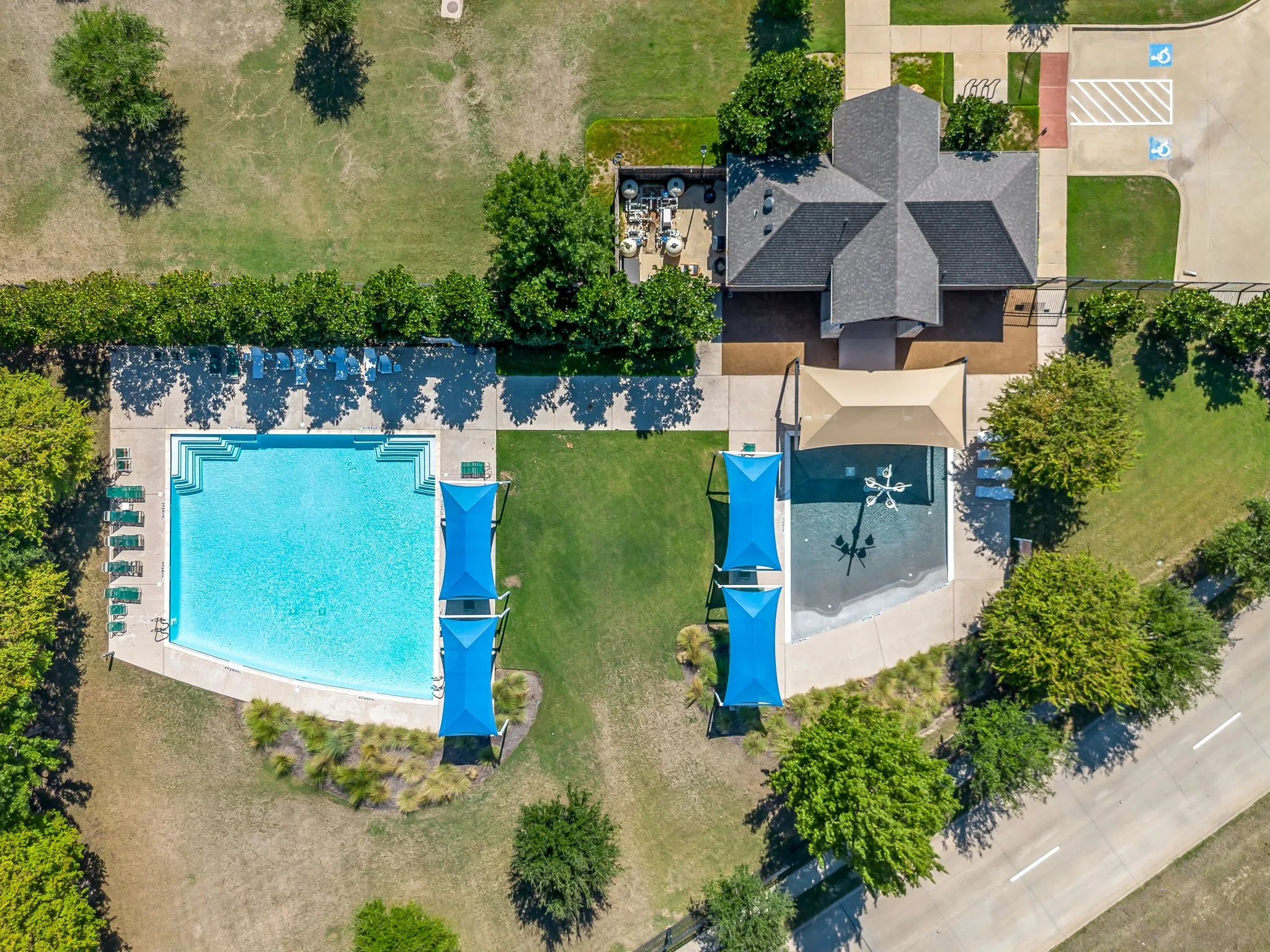 Expansive community pool with integrated steps, adjacent splash pad, and a shaded pergola structure