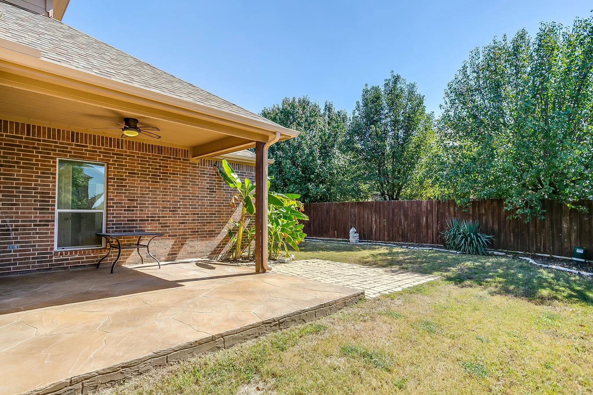 Covered patio with a ceiling fan, brick exterior, concrete patio flooring, paved walkway, and a wooden privacy fence