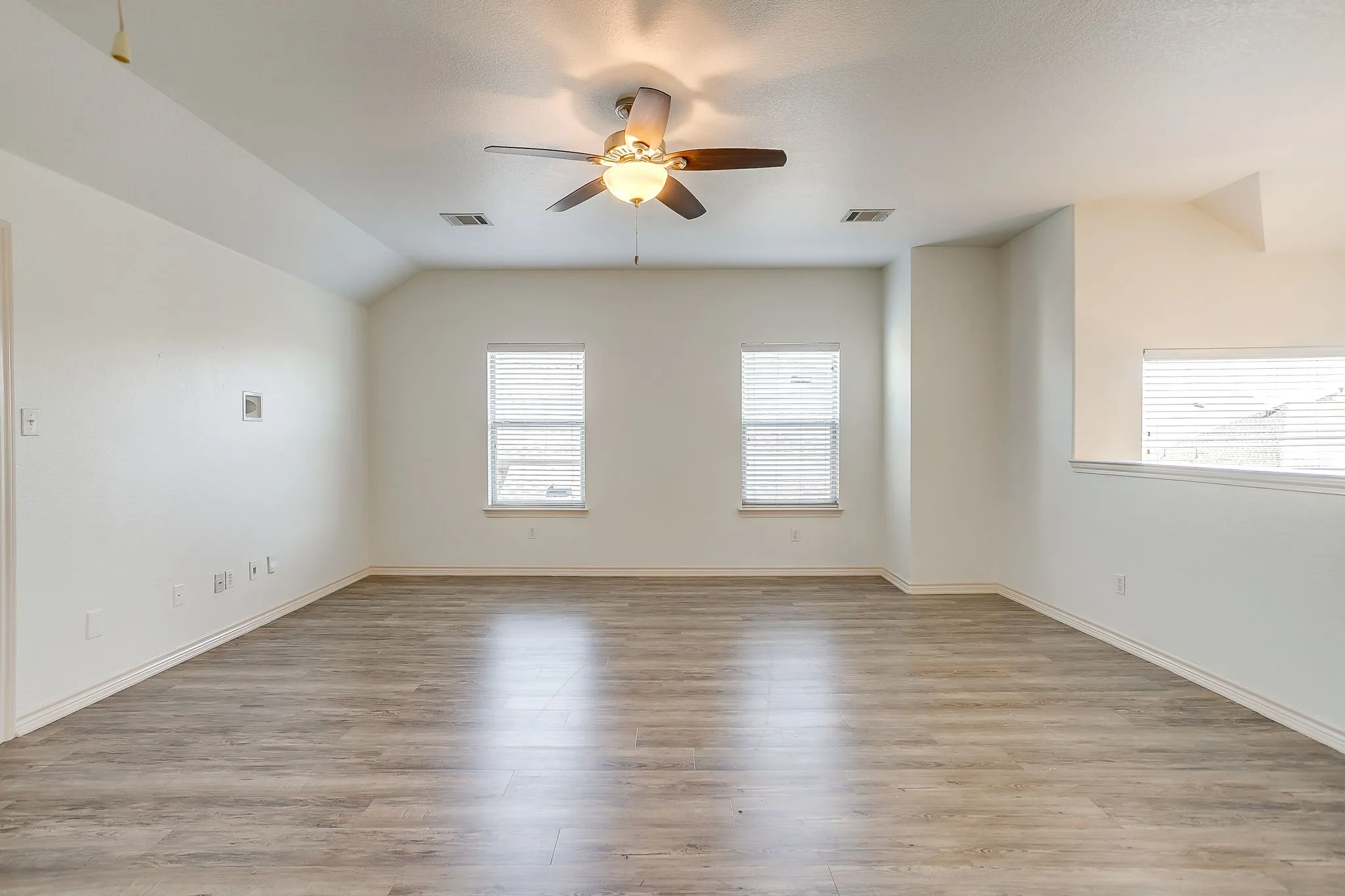 Vaulted ceiling with a ceiling fan, wood-finish flooring, multiple windows with blinds, and white walls