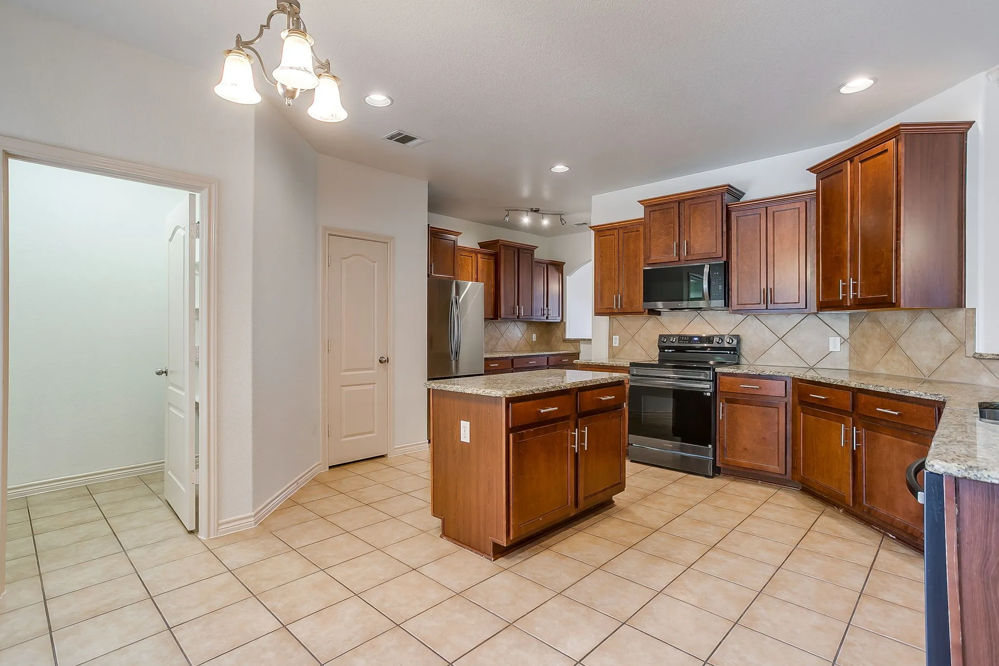 Kitchen featuring a central island, wood-finish cabinetry, tile flooring, stainless steel appliances, and recessed lighting
