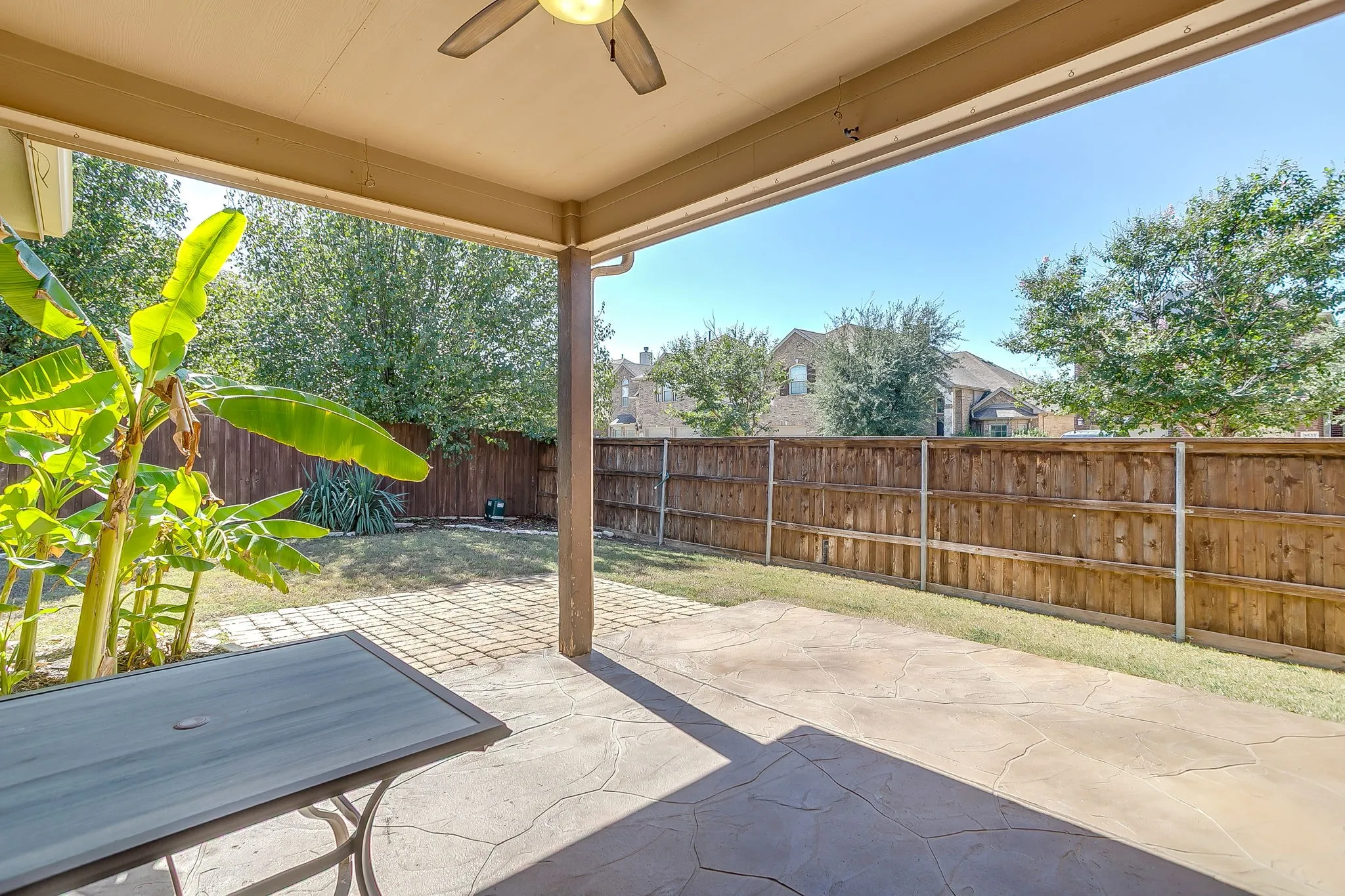Covered patio with an integrated ceiling fan, stamped concrete flooring, and a privacy fence enclosing the backyard