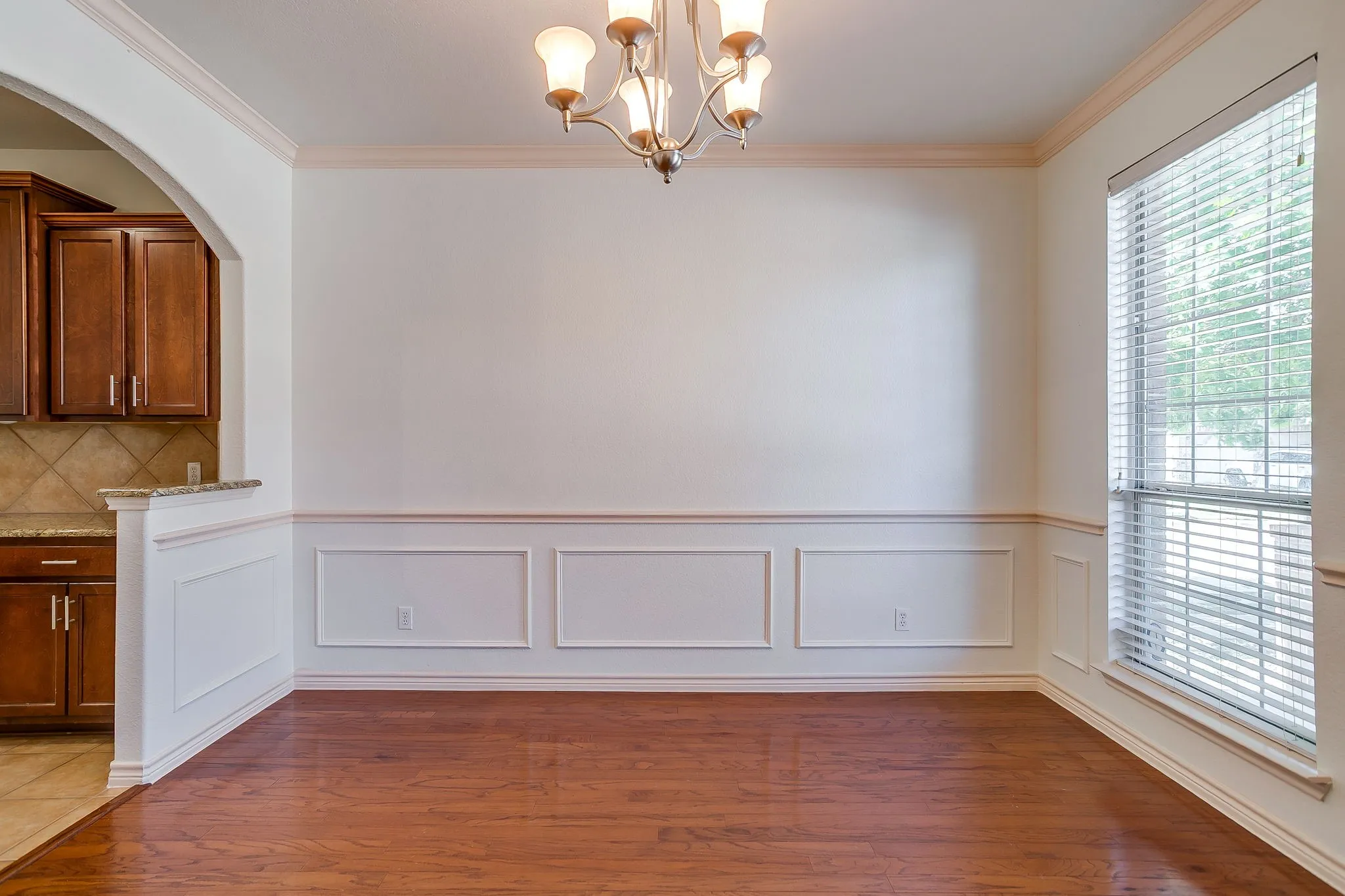 Wood-finish flooring, decorative wall molding, window with blinds, decorative ceiling light fixture, and arched doorway