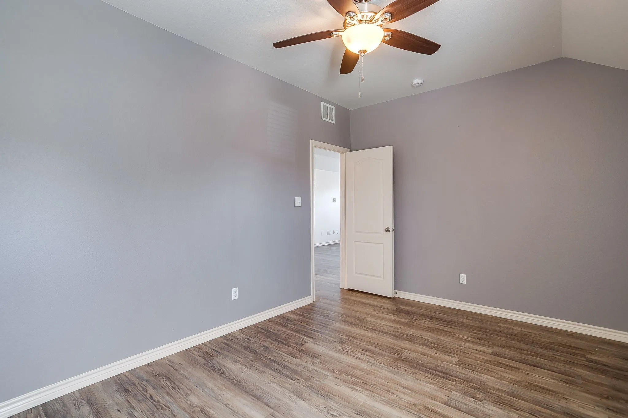 Wood-finish flooring with white trim and a ceiling fan with integrated lighting