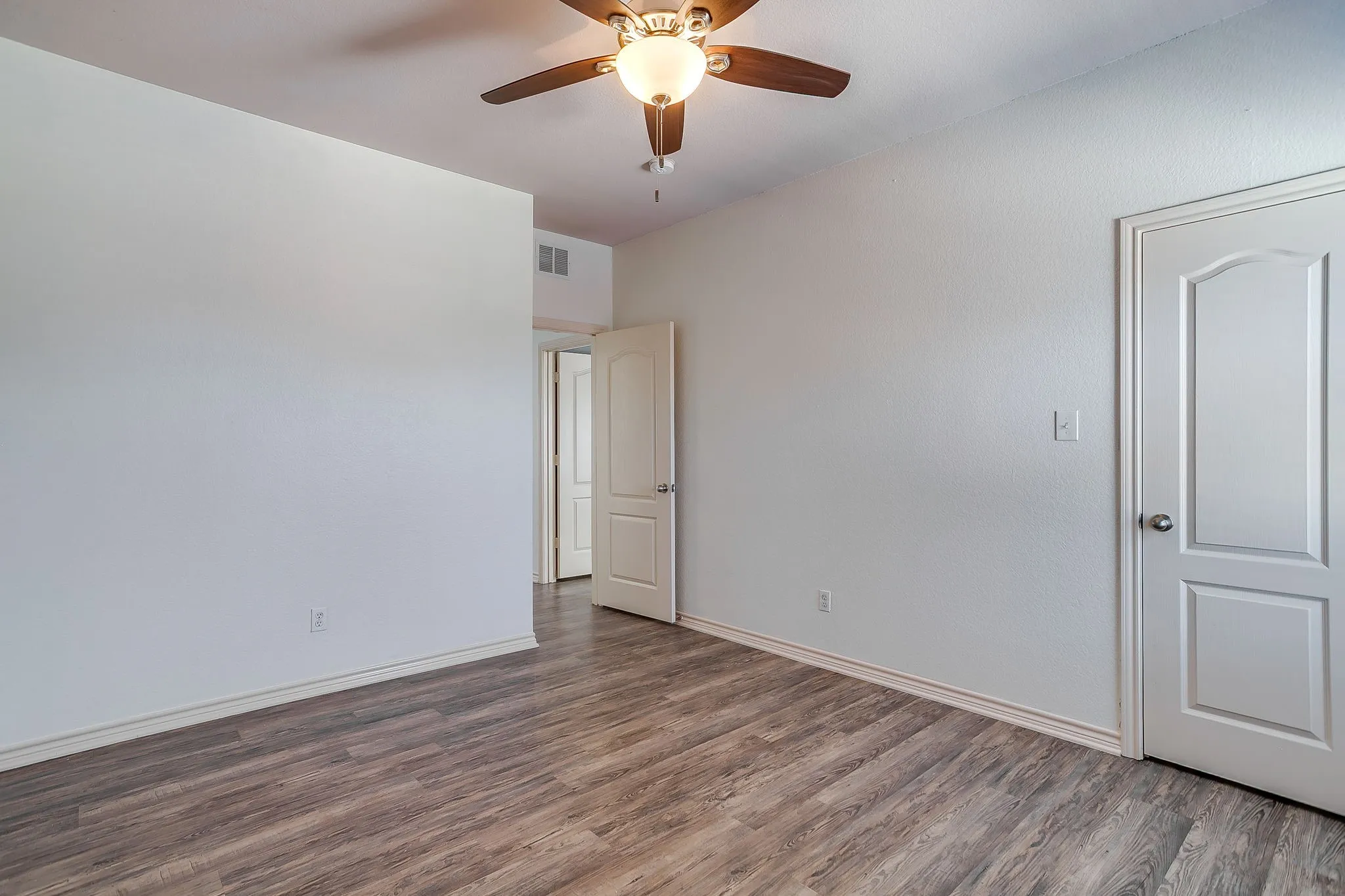 Spacious bedroom featuring wood-finish flooring, ceiling fan with integrated lighting, and dual closet access