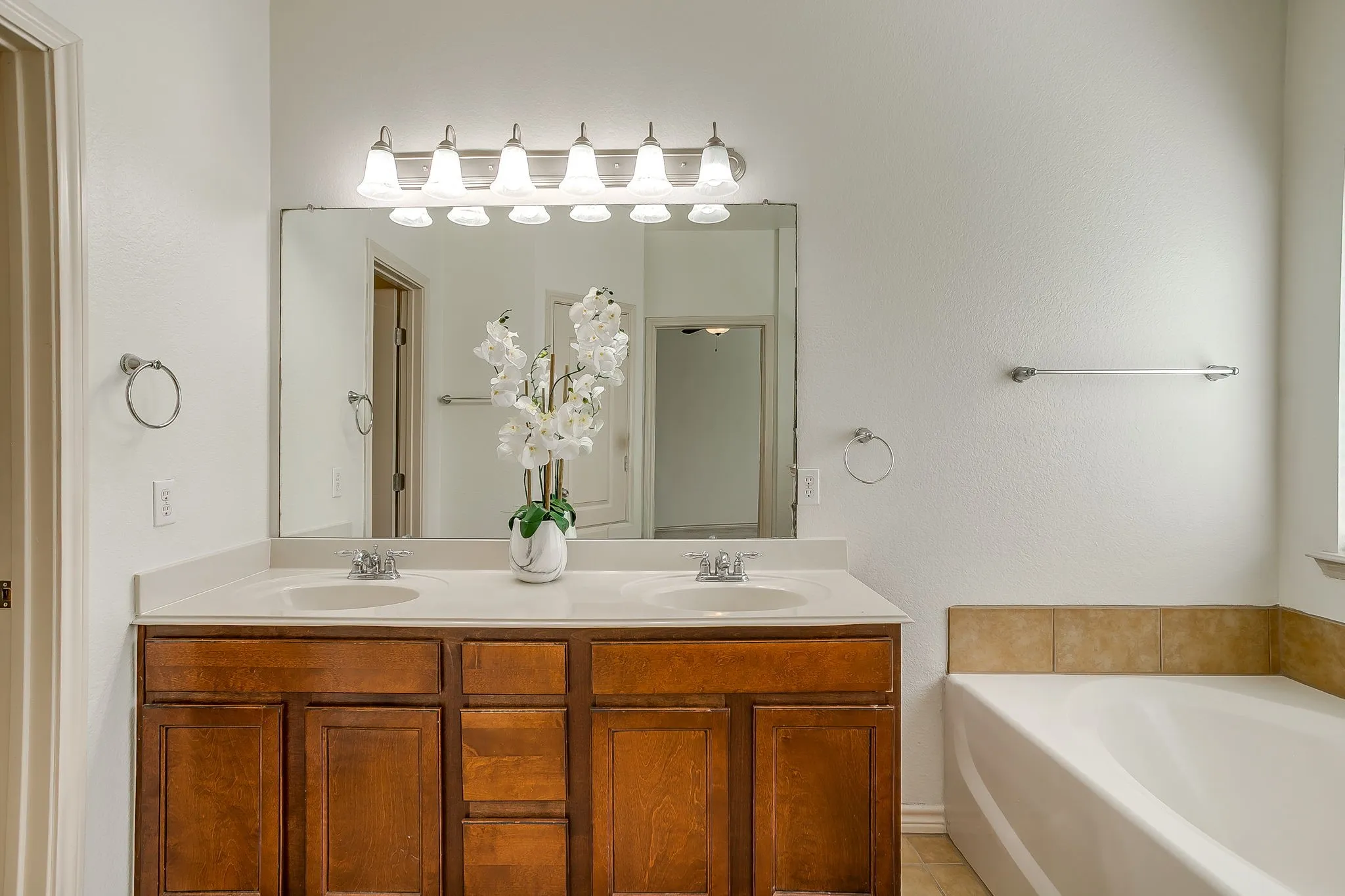 Dual sink vanity with wood-finish cabinetry, a framed mirror, and an overhead light fixture