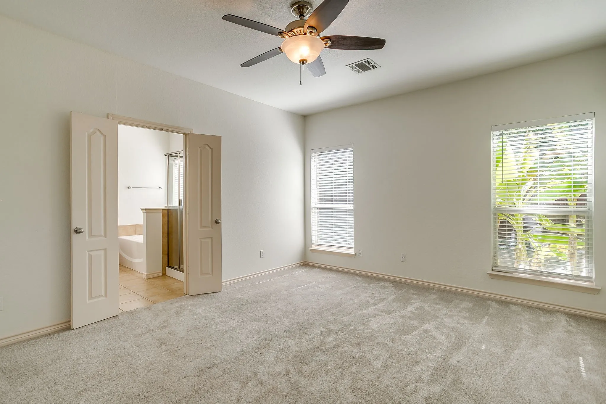 Spacious room featuring light gray carpeting, a ceiling fan with integrated lighting, and two windows with white blinds
