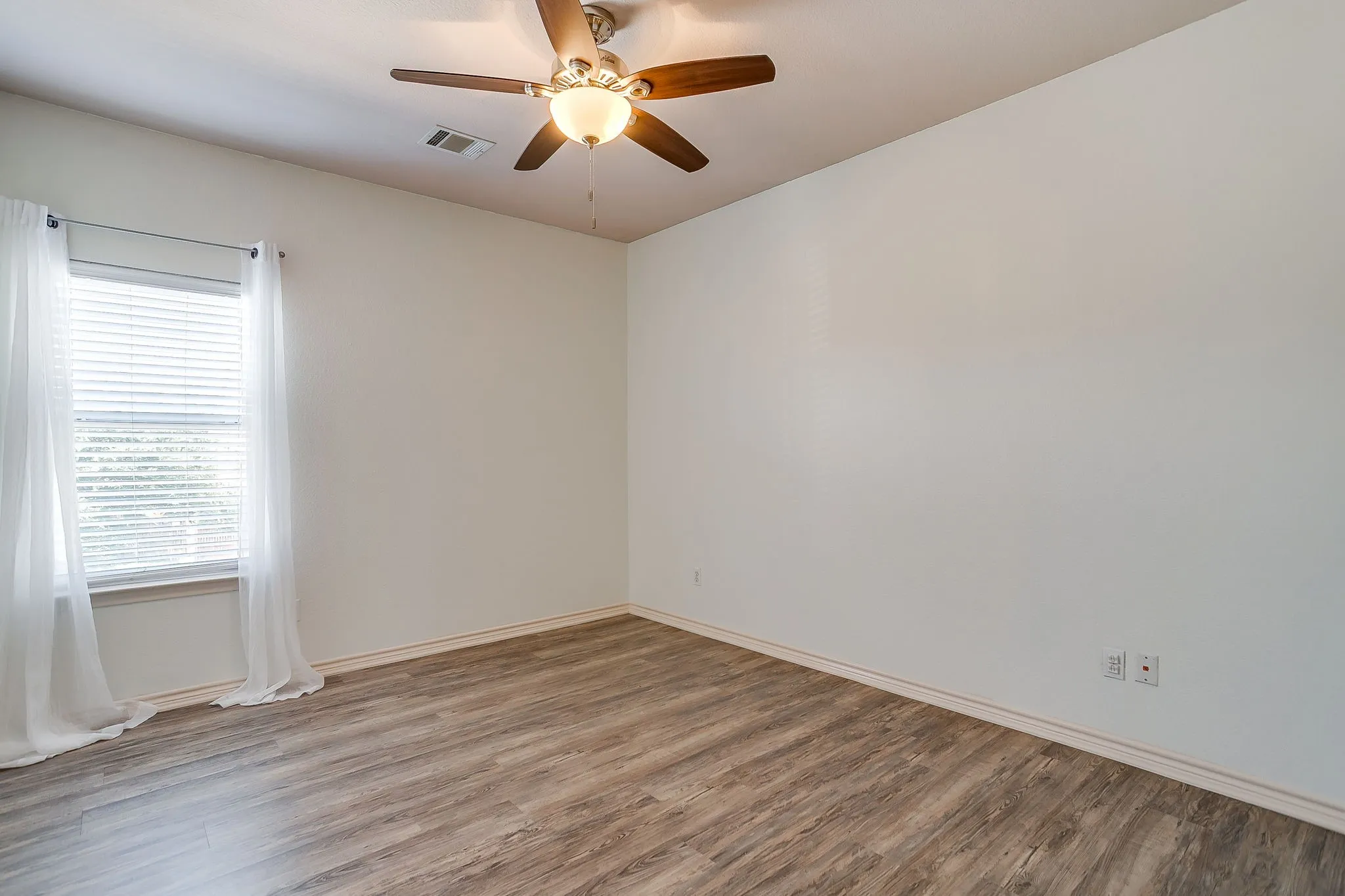 Wood-finish flooring, white walls, ceiling fan with integrated lighting, and a window with blinds