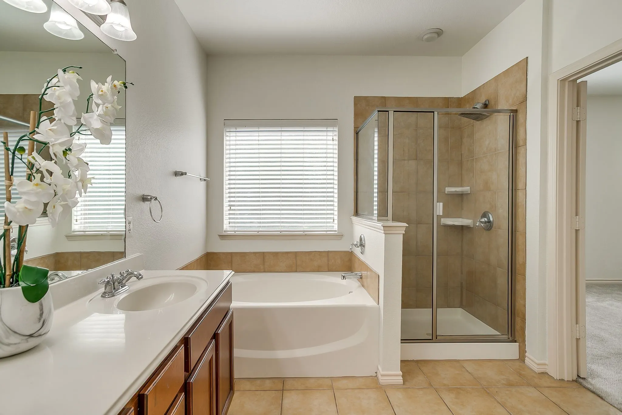 Dual sink vanity with white countertop, soaking tub, glass-enclosed shower, and tiled flooring