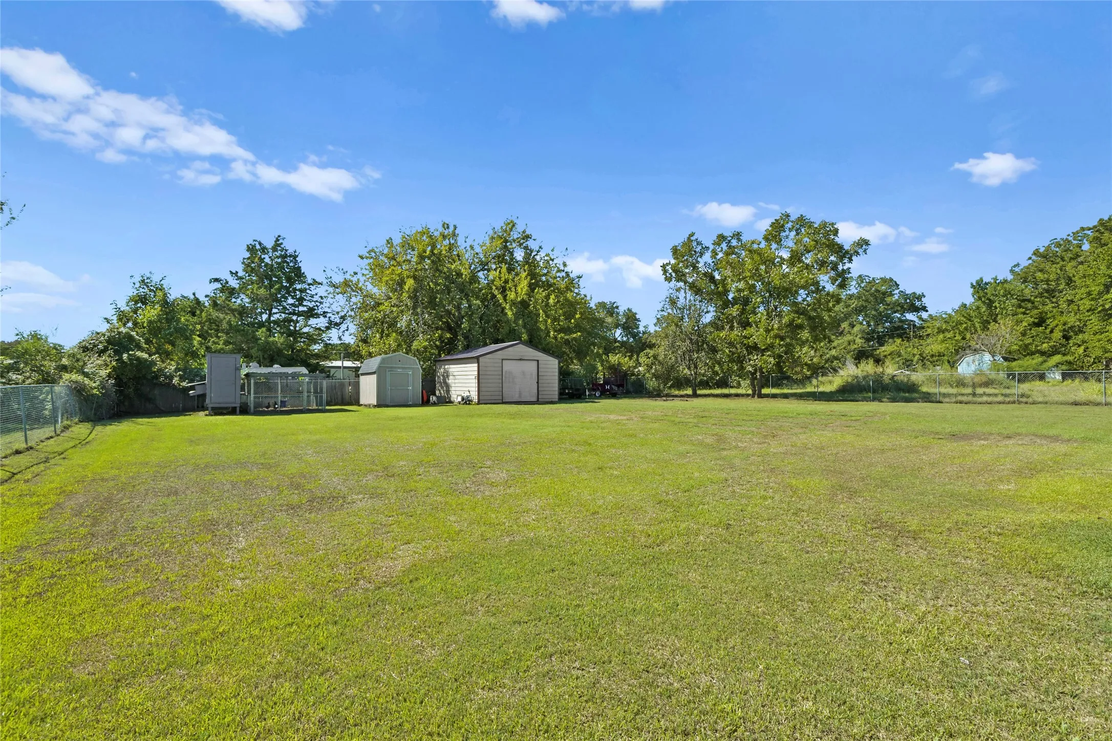Expansive green lawn with established trees, featuring two storage sheds and a chain-link fence