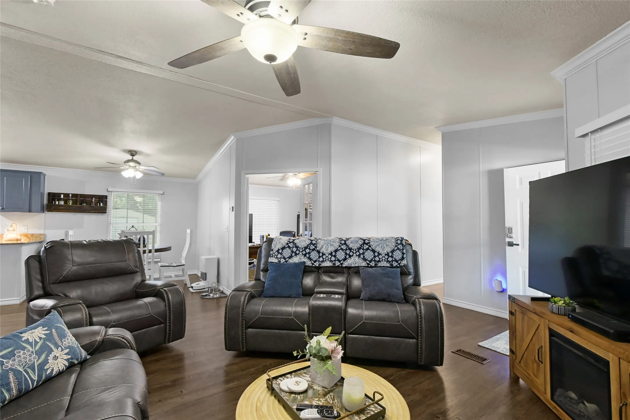 Spacious open-concept living area featuring hardwood flooring, ceiling fans with integrated lighting, and a wood-finish entertainment center