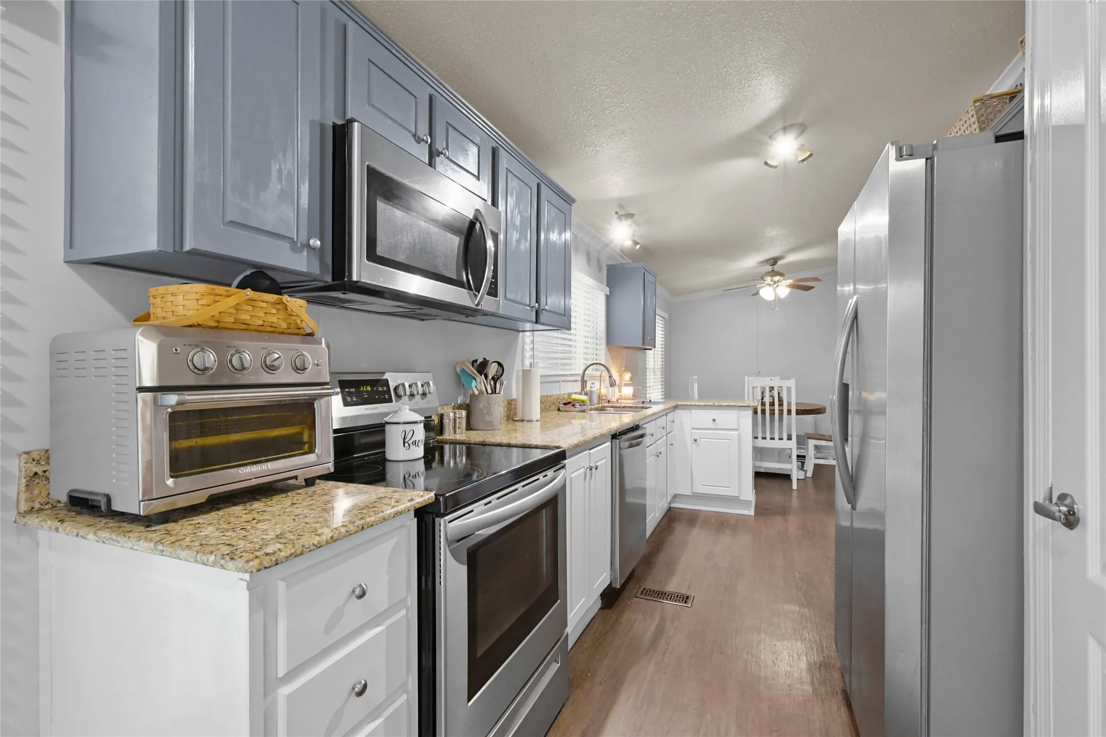 Kitchen featuring wood-finish flooring, light-toned countertops, stainless steel appliances, and two-tone cabinetry