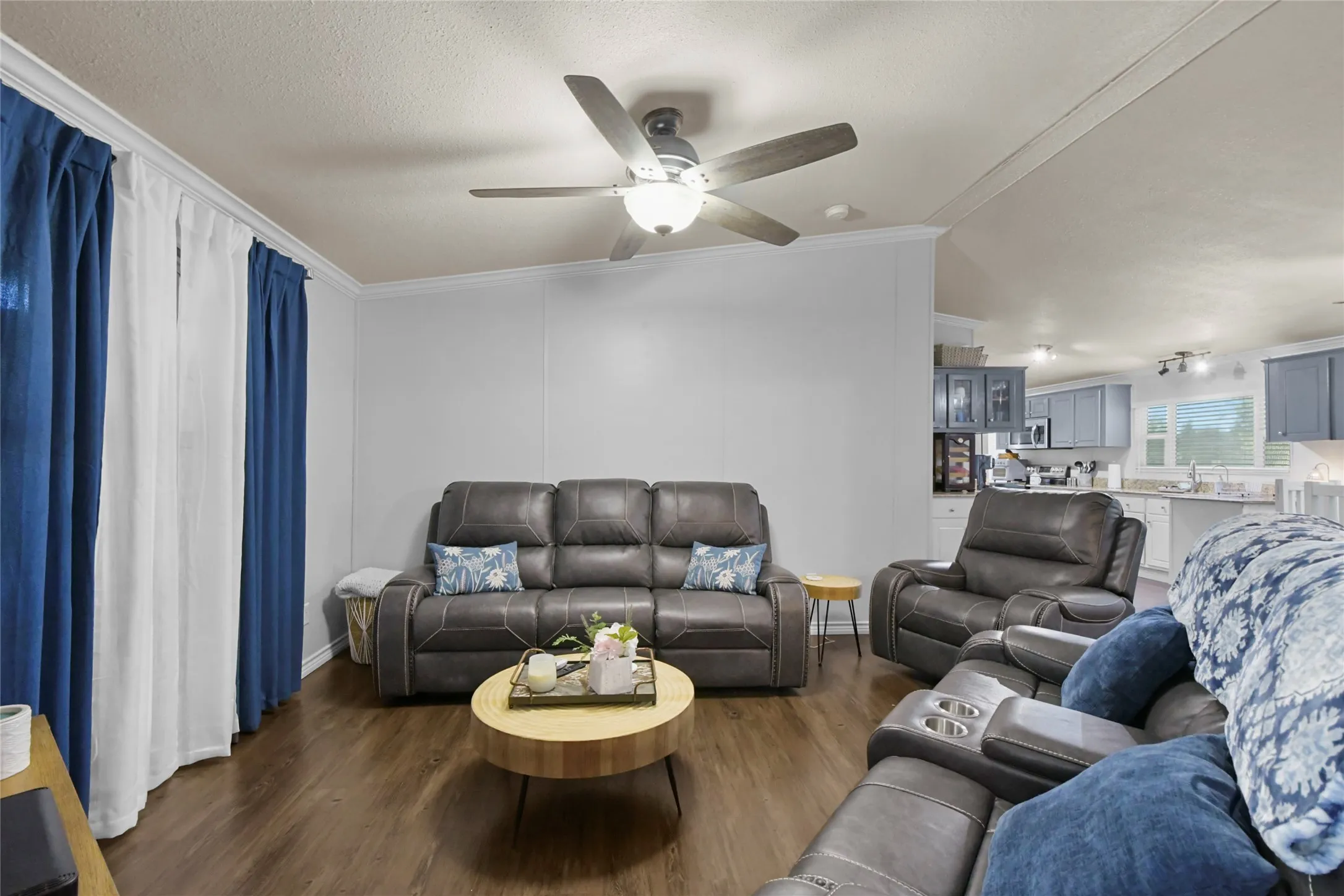Spacious living area featuring wood-finish flooring throughout, a ceiling fan with integrated lighting, and comfortable seating arrangements