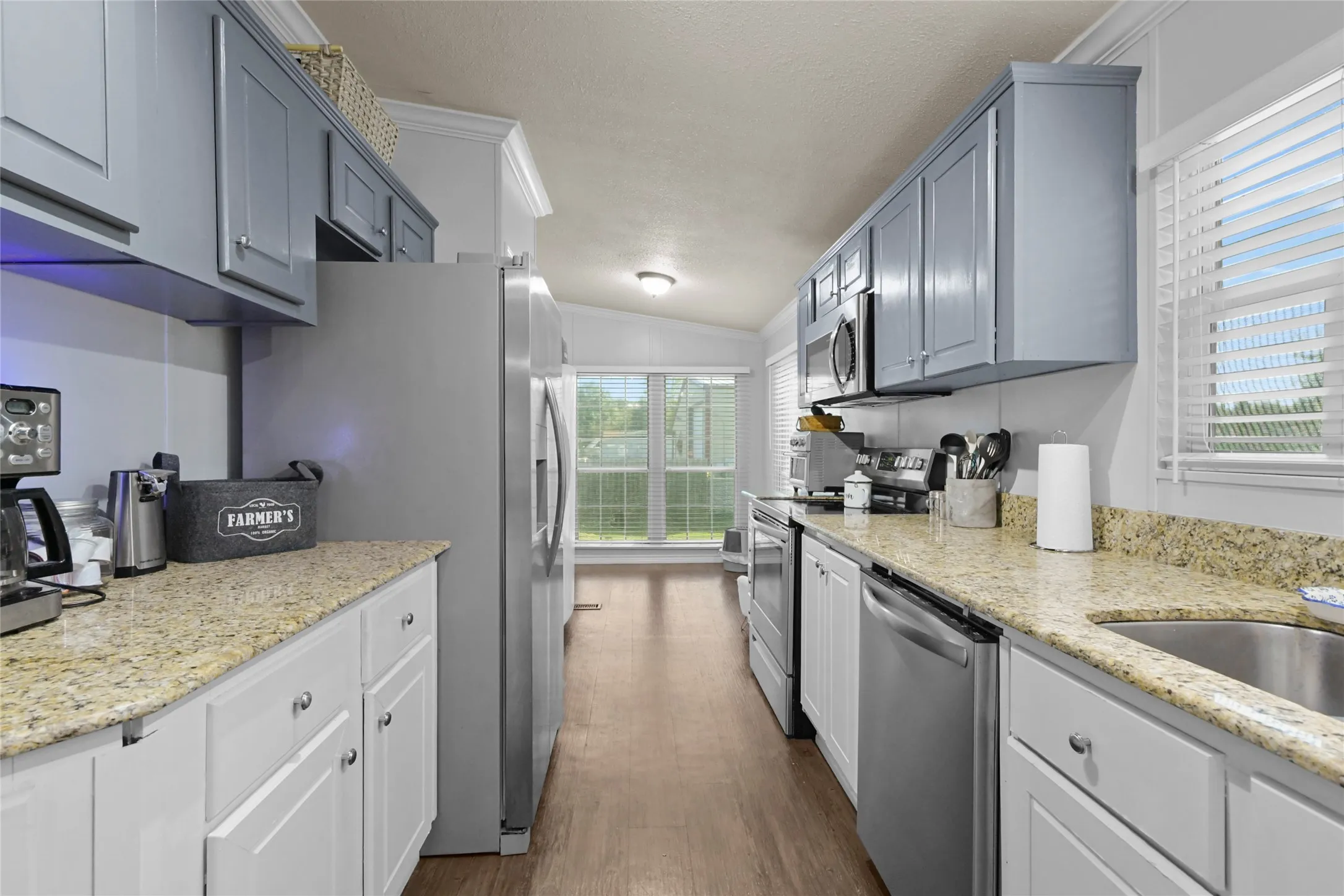 Galley kitchen featuring granite-style countertops, stainless steel appliances, and dual-tone cabinetry
