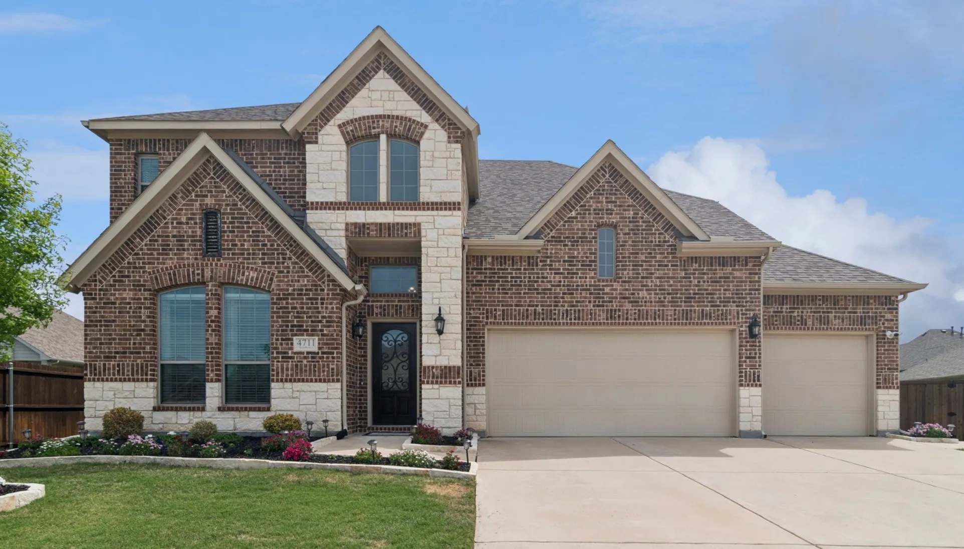 Brick and stone facade, arched windows, covered entry, dual garage doors, paved driveway