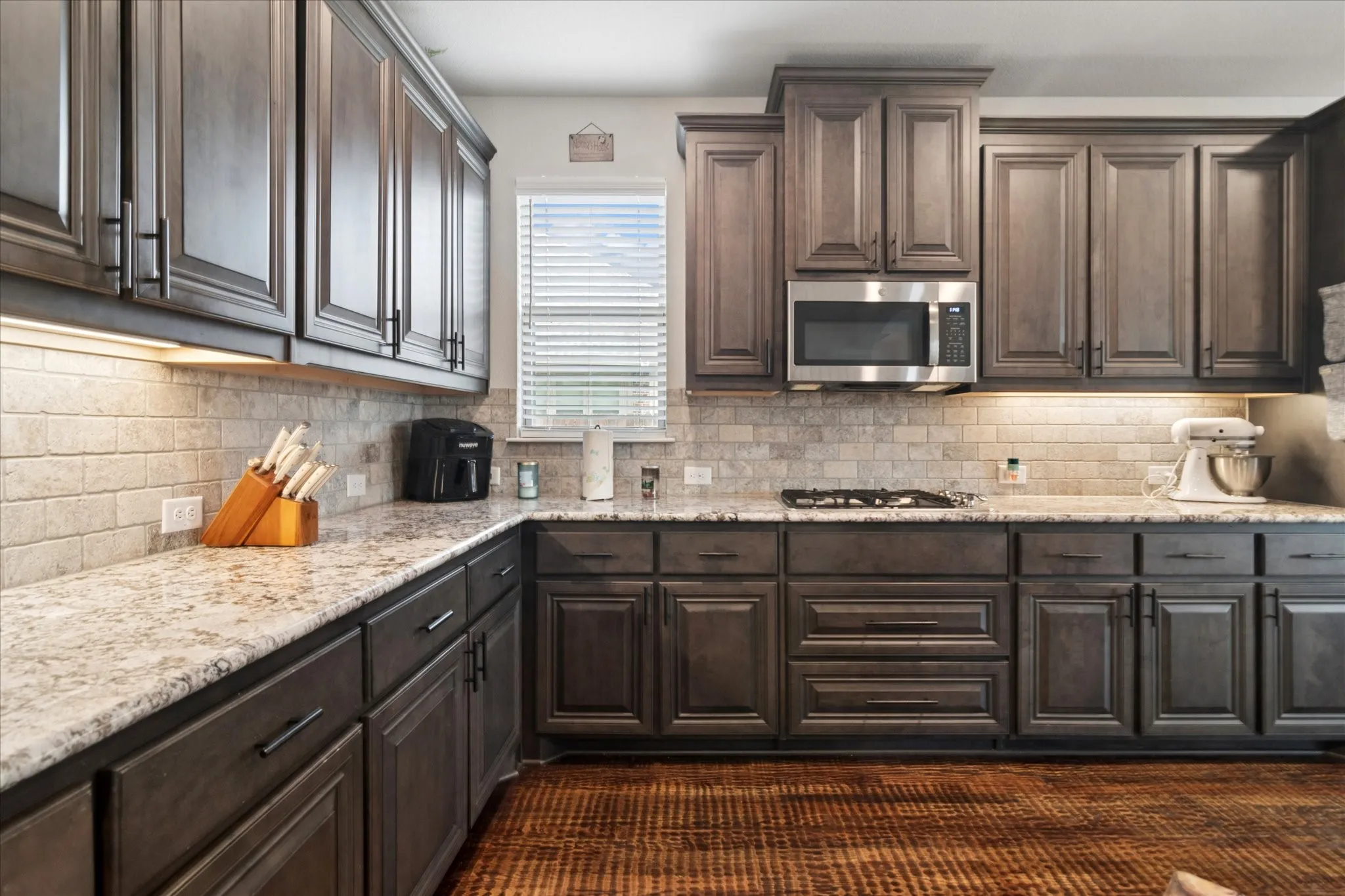 Extensive cabinetry with dark finishes, stone countertops, tiled backsplash, stainless steel microwave, and integrated cooktop
