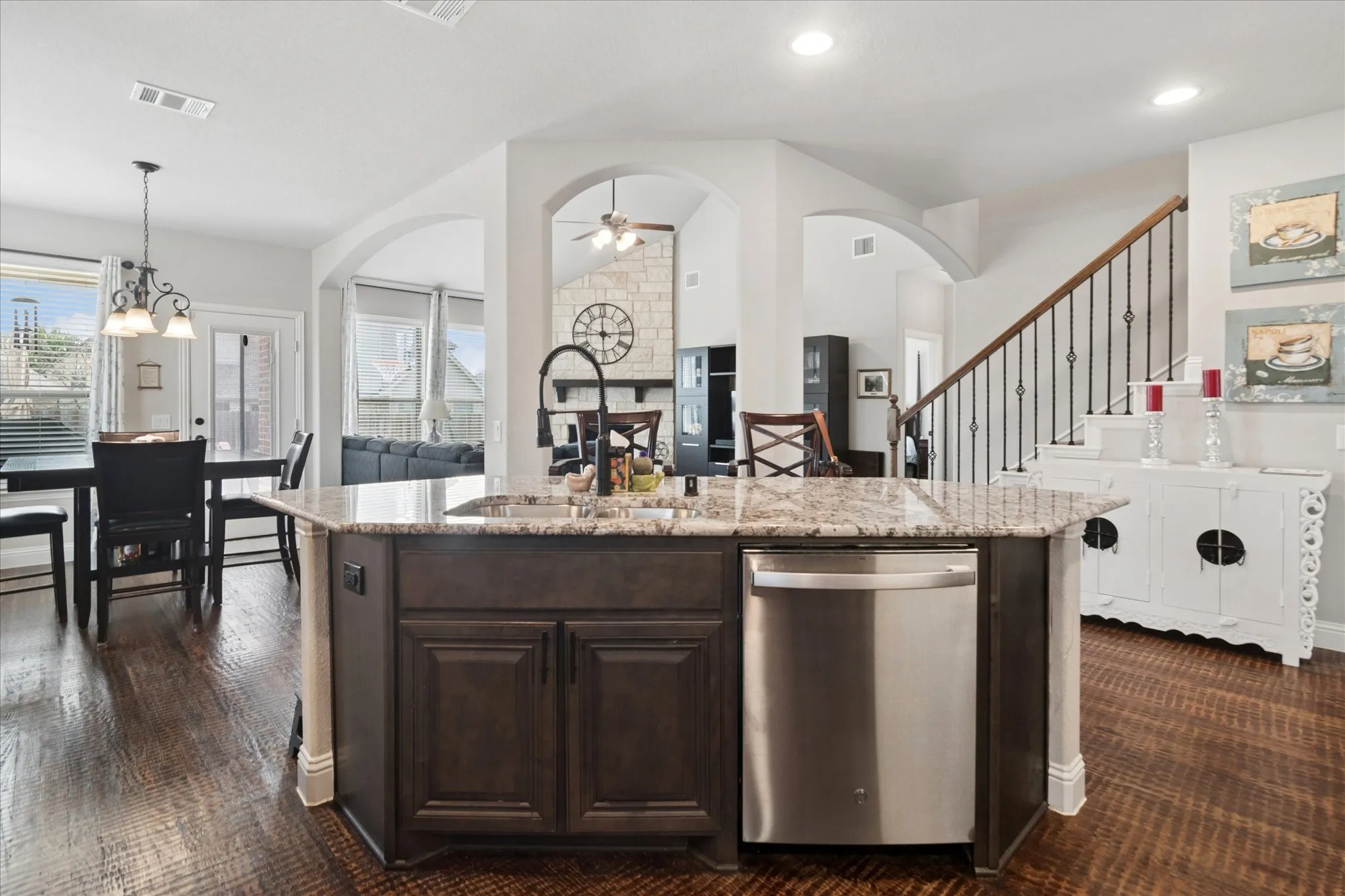 Kitchen island with granite countertop, integrated stainless steel dishwasher, and dark wood-finish cabinetry