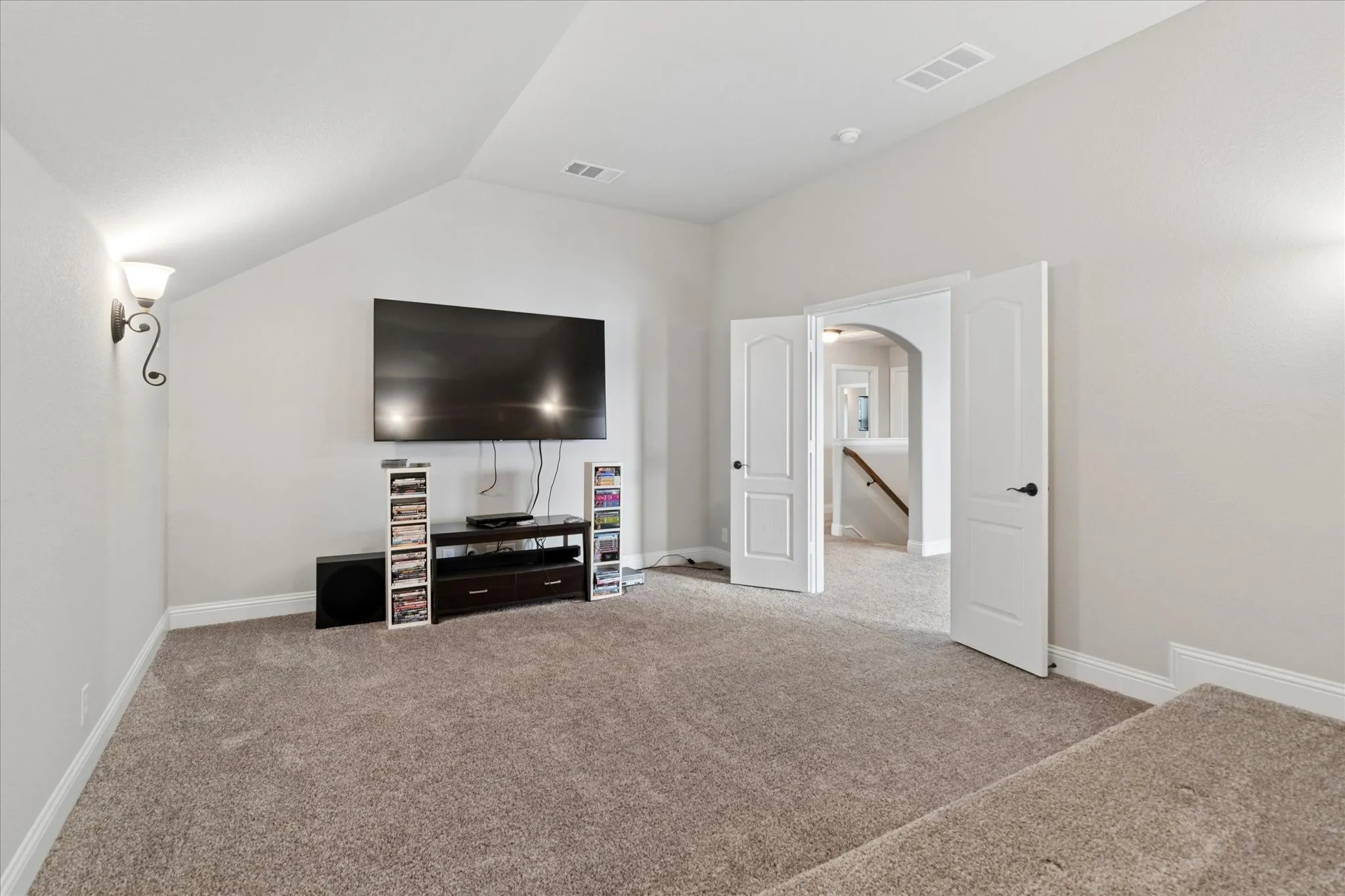 Carpeted room with sloped ceiling, two wall sconces, and an arched doorway