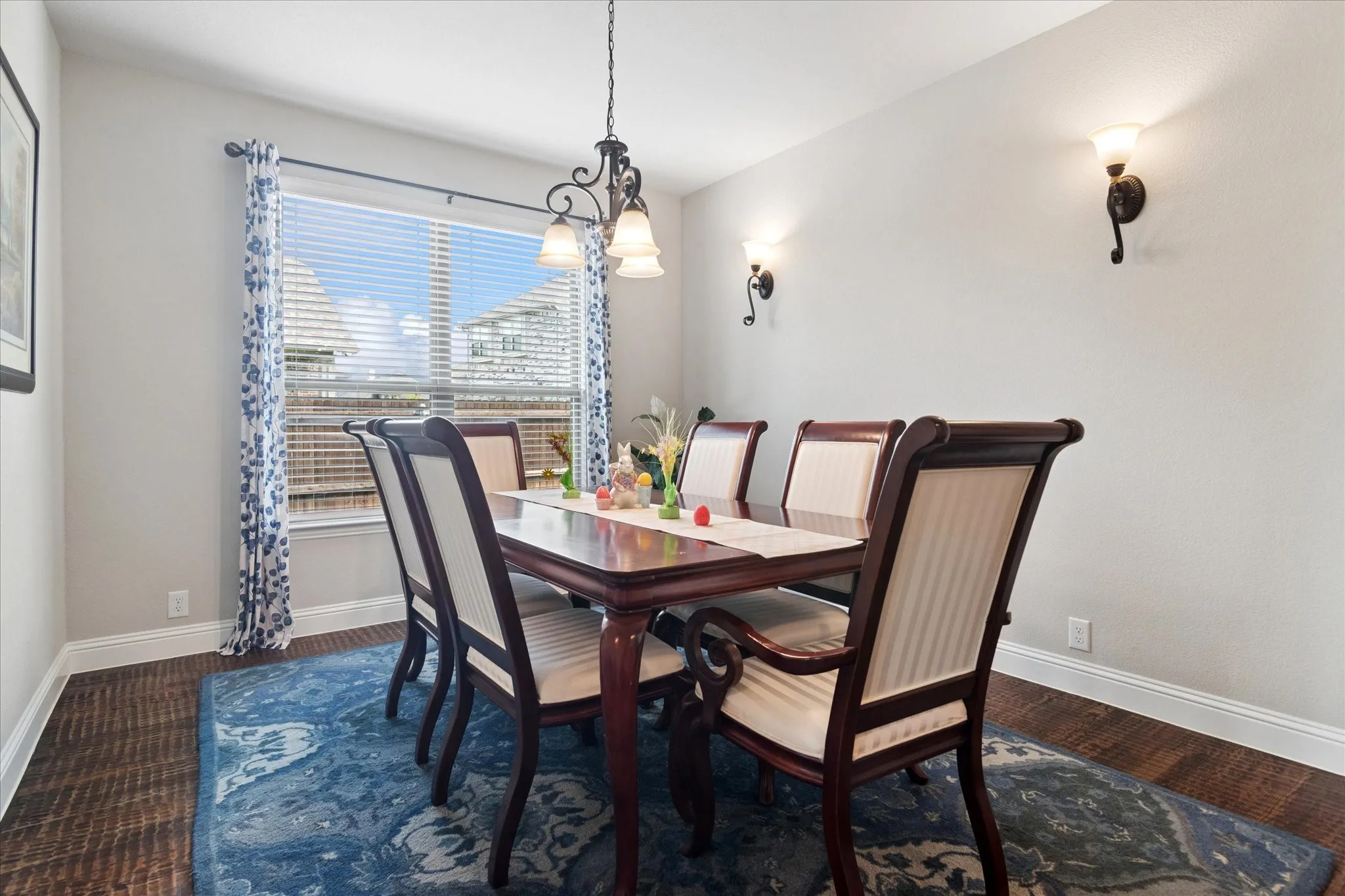 Expansive window with blinds, wood-finish flooring, chandelier lighting, and two wall sconces