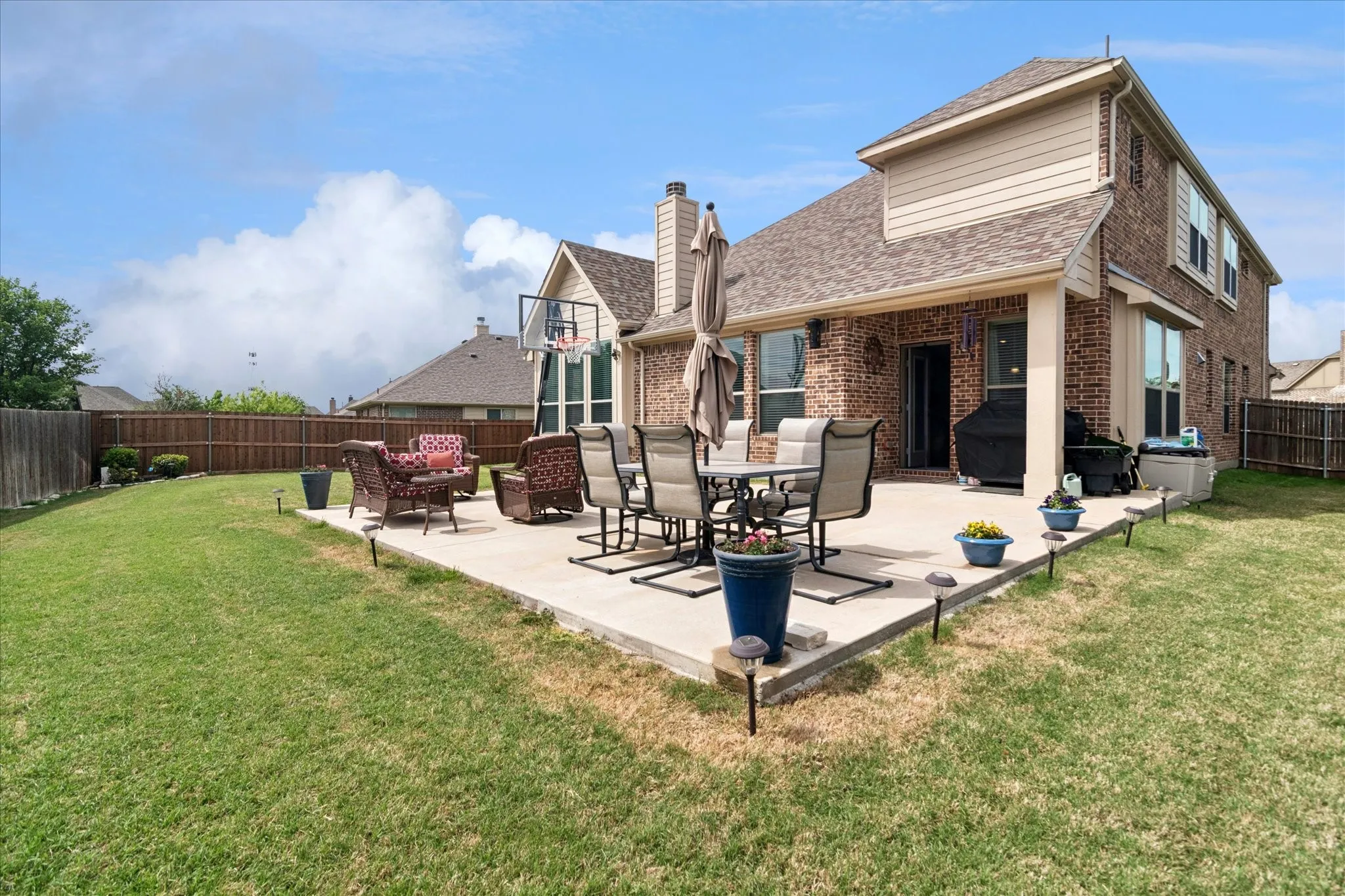 Expansive backyard featuring a manicured lawn, full privacy fencing, and a concrete patio with a covered section