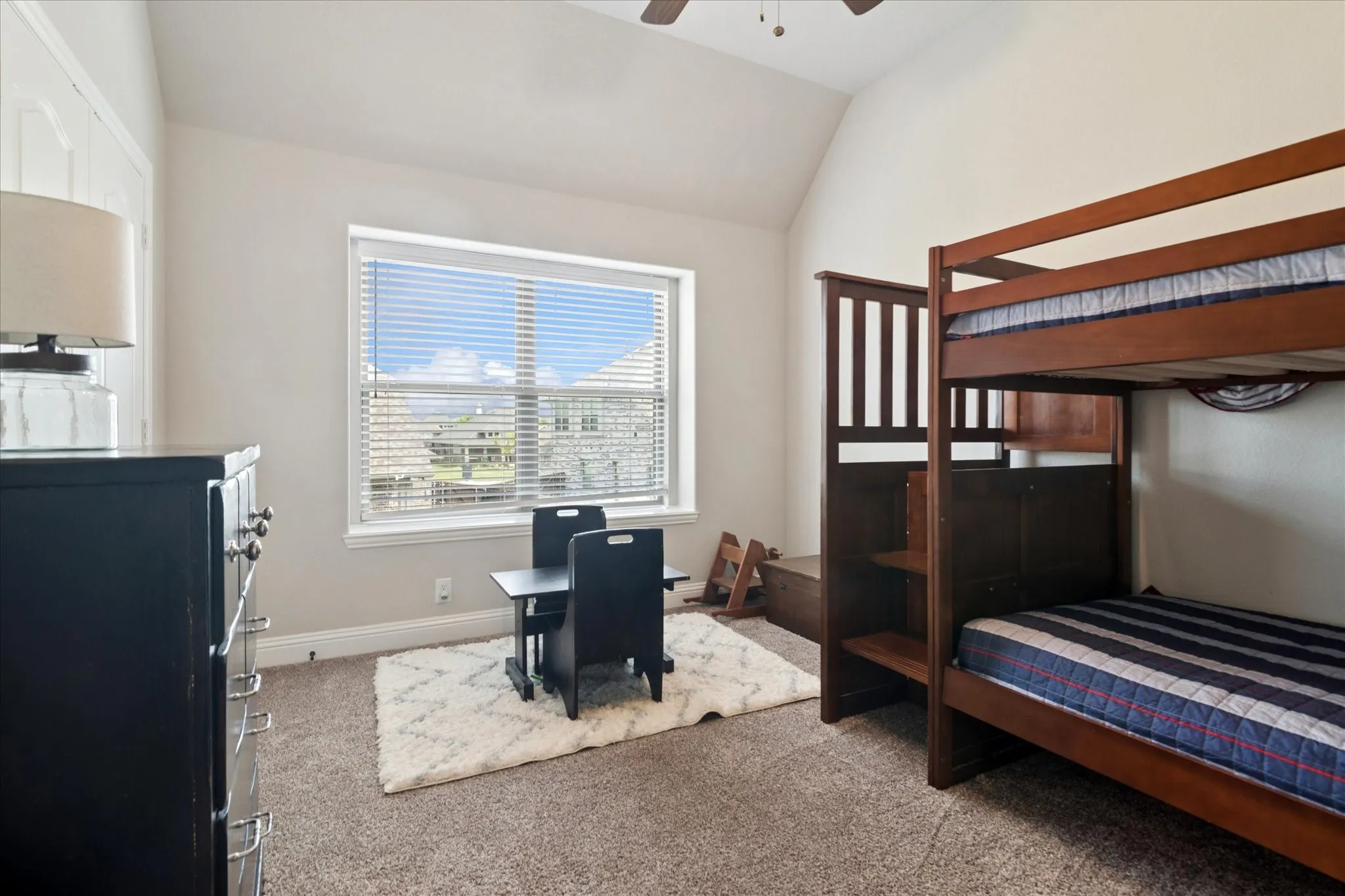 Neutral wall color, vaulted ceiling, large window with blinds, and carpeted flooring