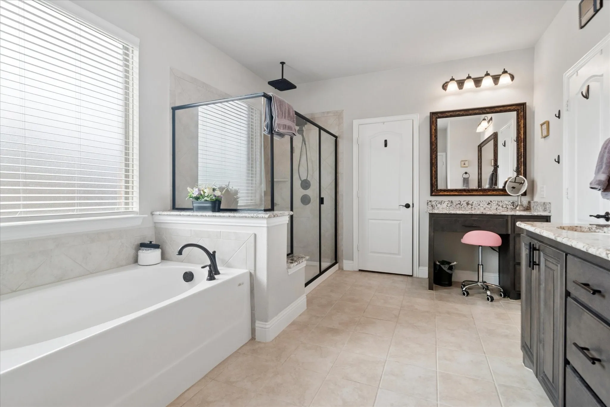 Spacious bathroom featuring a built-in soaking tub, a separate glass-enclosed shower, a double vanity with stone countertops, and tile flooring
