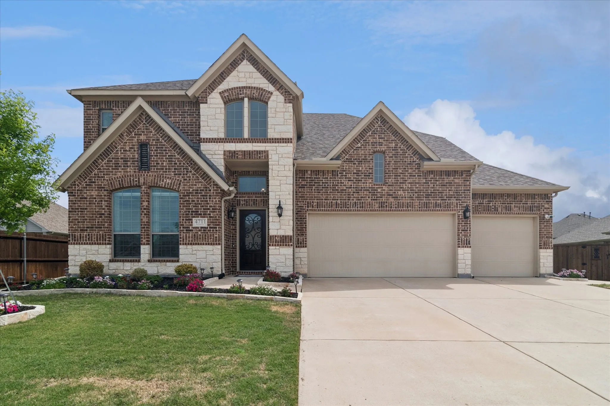 Brick and stone façade with arched windows, prominent gables, and a three-car garage