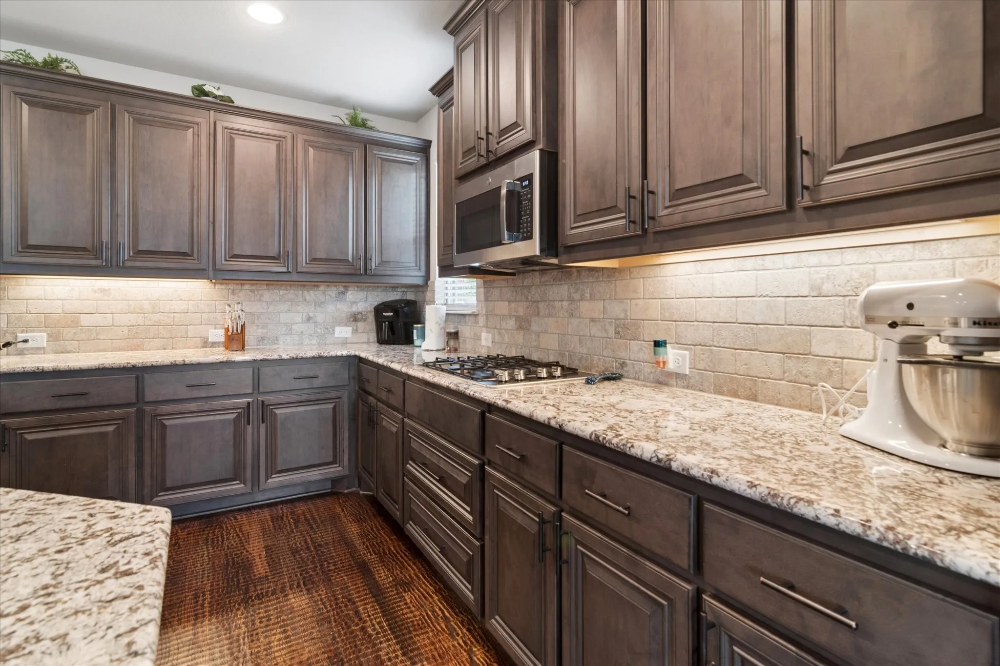 Full-height cabinetry, granite countertops, tile backsplash, built-in microwave, and a gas cooktop