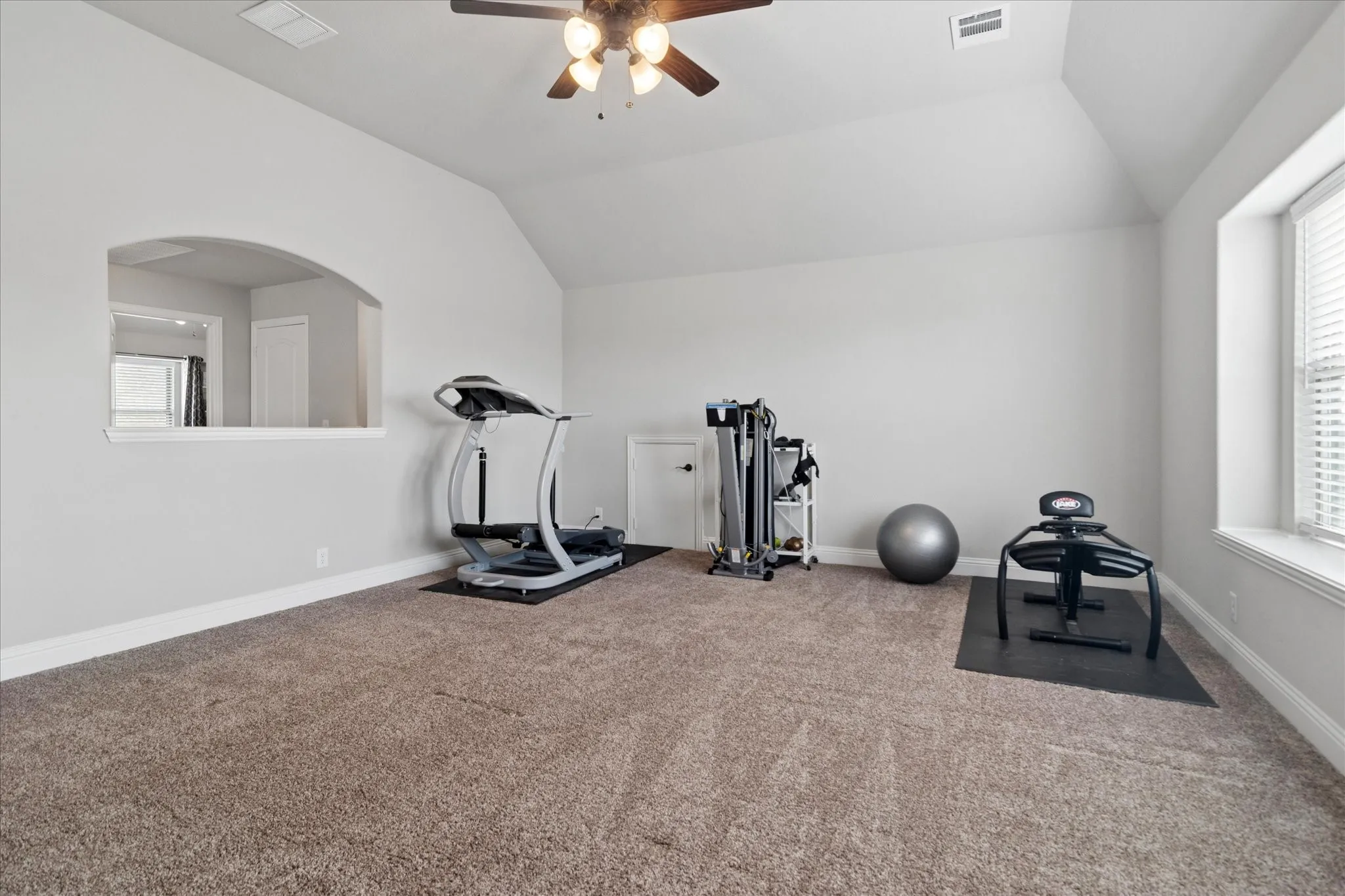 Vaulted ceiling with a ceiling fan, carpeted flooring, window with blinds, and an arched interior opening