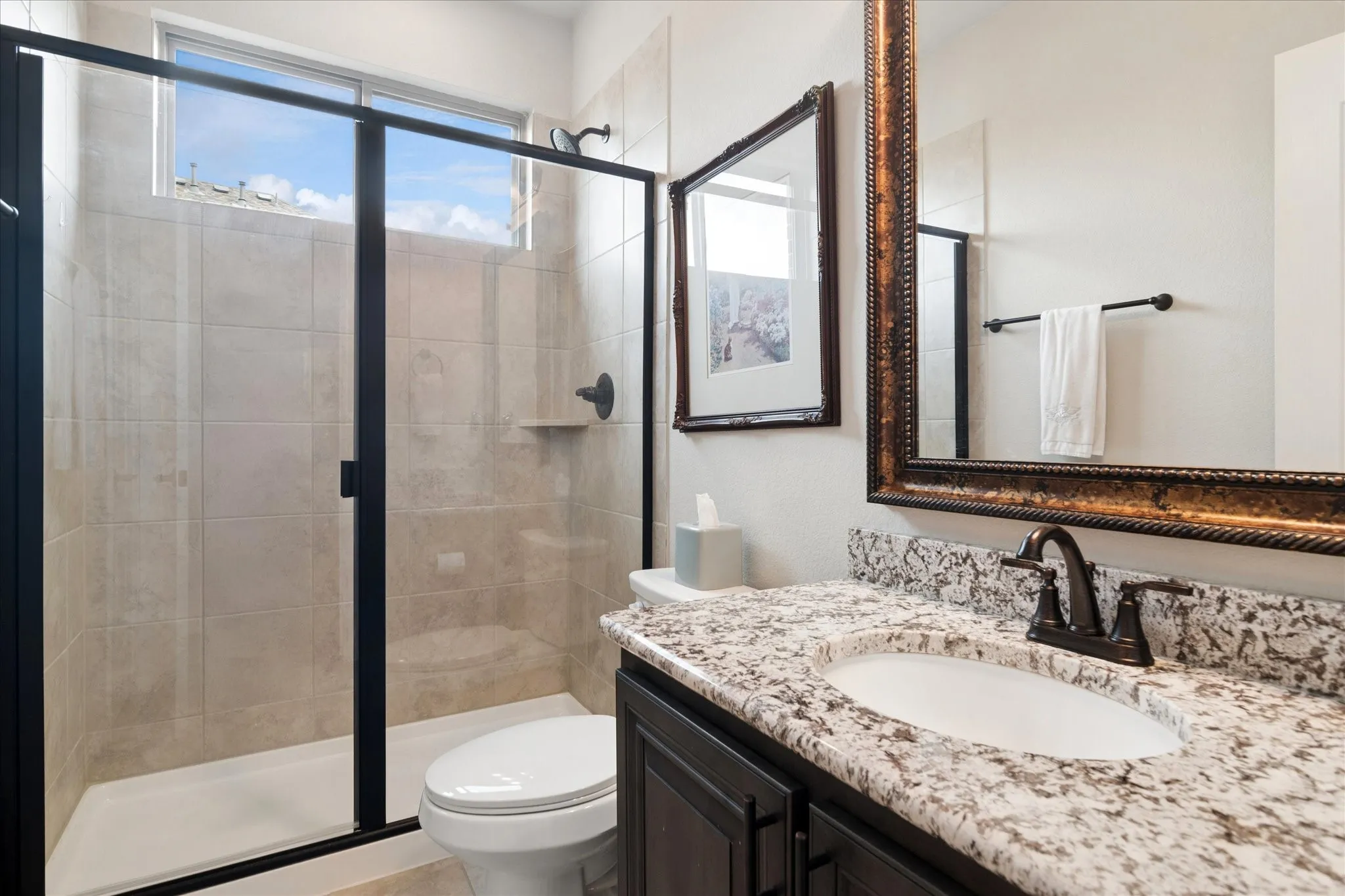 Shower with clear glass enclosure and dark trim, neutral tile surround, and a fixed transom window
