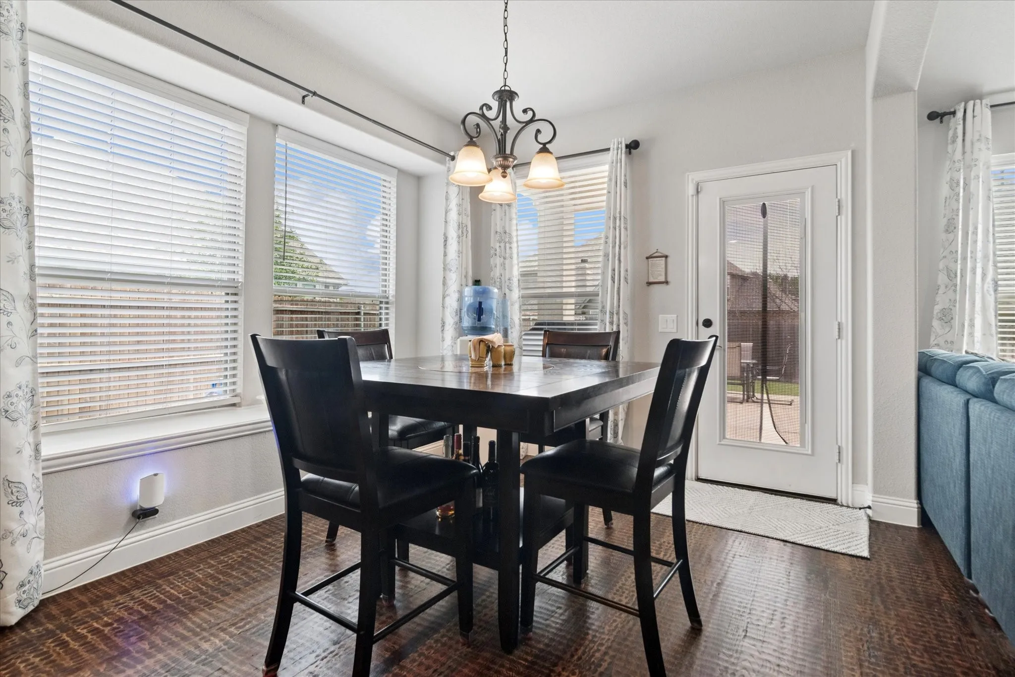 Wood-finish flooring, multiple windows with blinds, a glass-panel door, and an ornate pendant light fixture