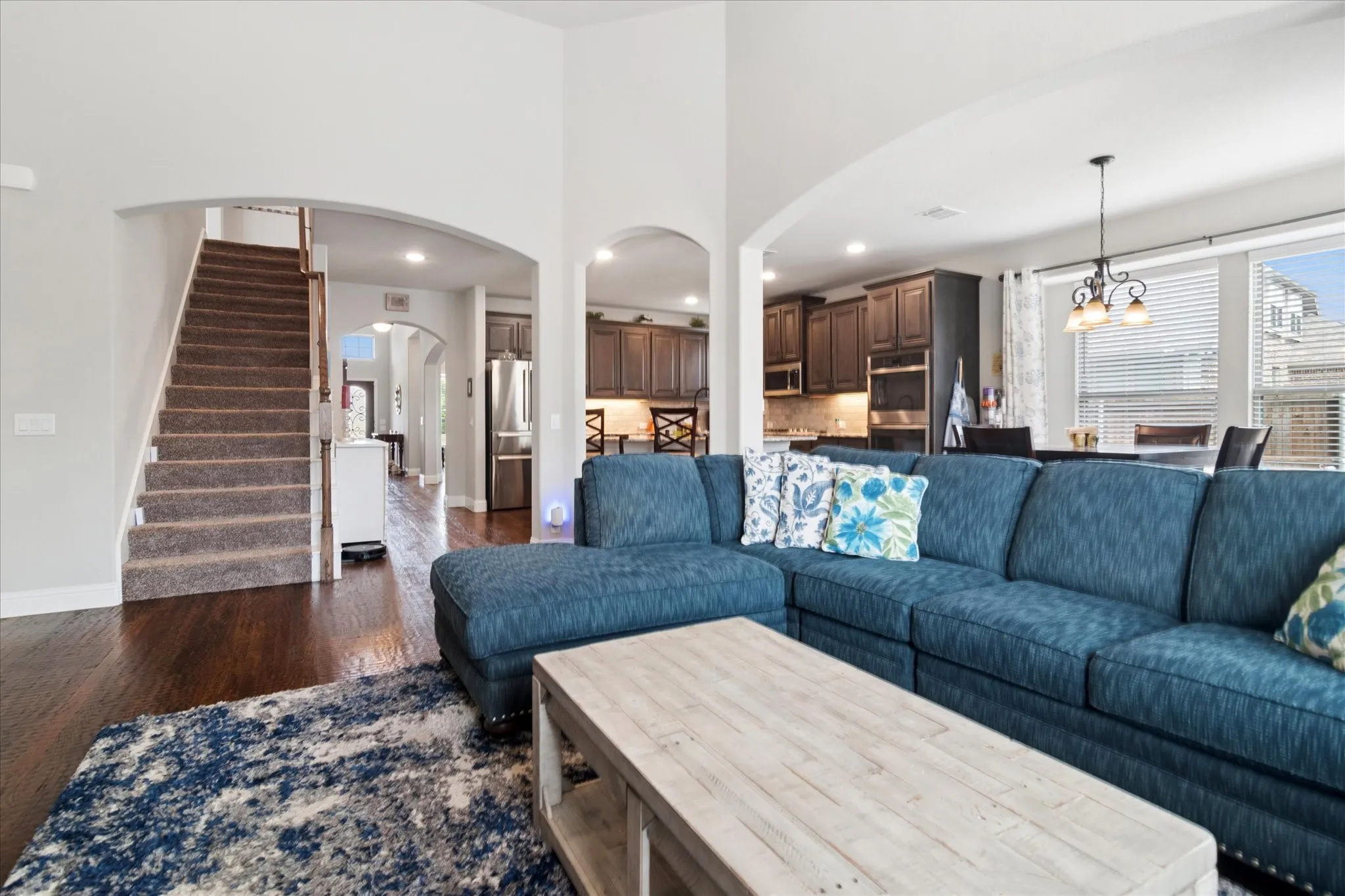 Hardwood-finish flooring, arched doorways, staircase with carpeted treads, built-in stainless steel appliances, and large windows with blinds