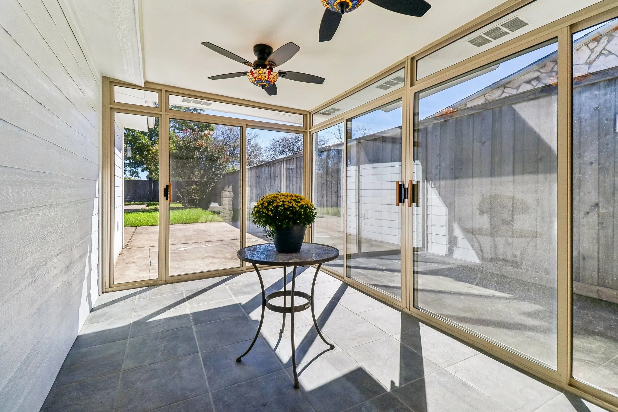 Sunroom featuring full-height sliding glass doors, tile flooring, two ceiling fans, and wood-paneled walls