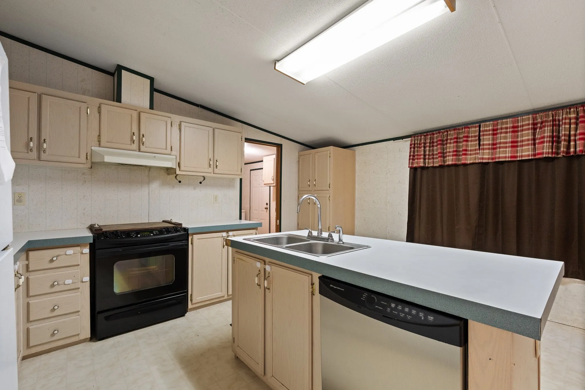 Kitchen with light colored cabinetry, electric stove with cooktop, plenty of counter space, dishwasher and sink.