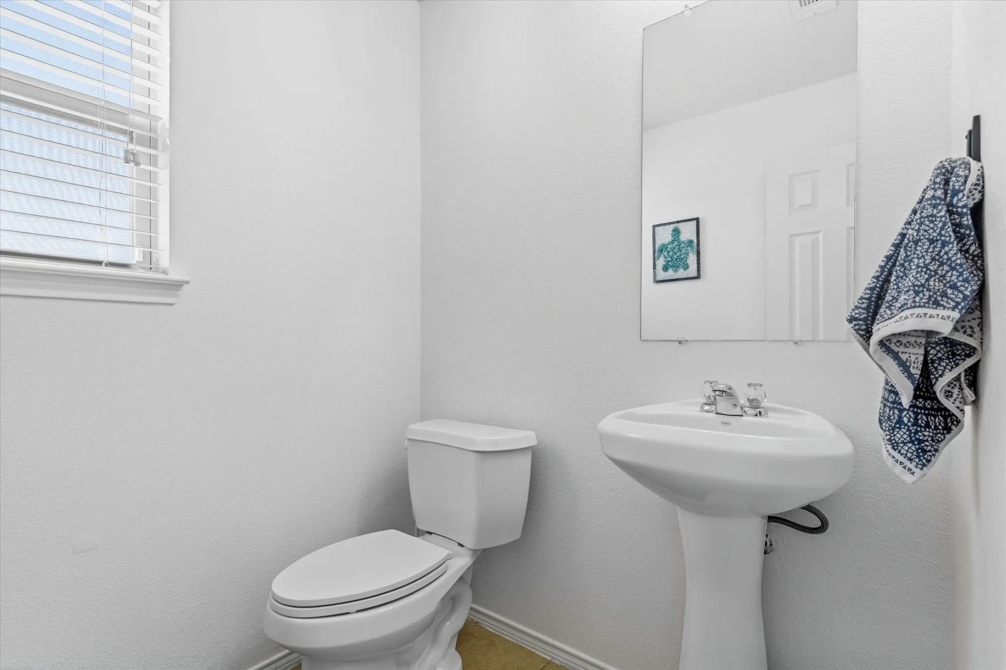 Pedestal sink with chrome faucet, toilet, and a rectangular mirror