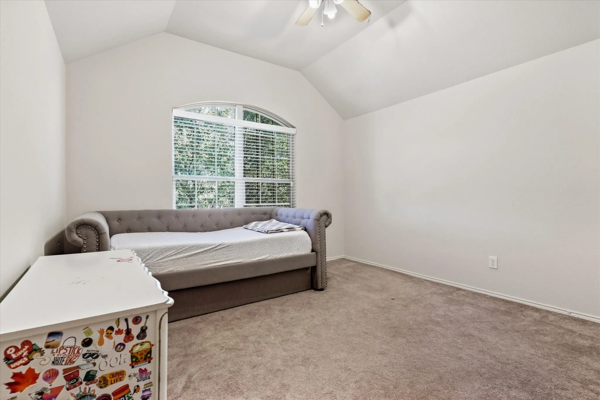 Vaulted ceiling with a ceiling fan, arched window with horizontal blinds, and neutral carpeting